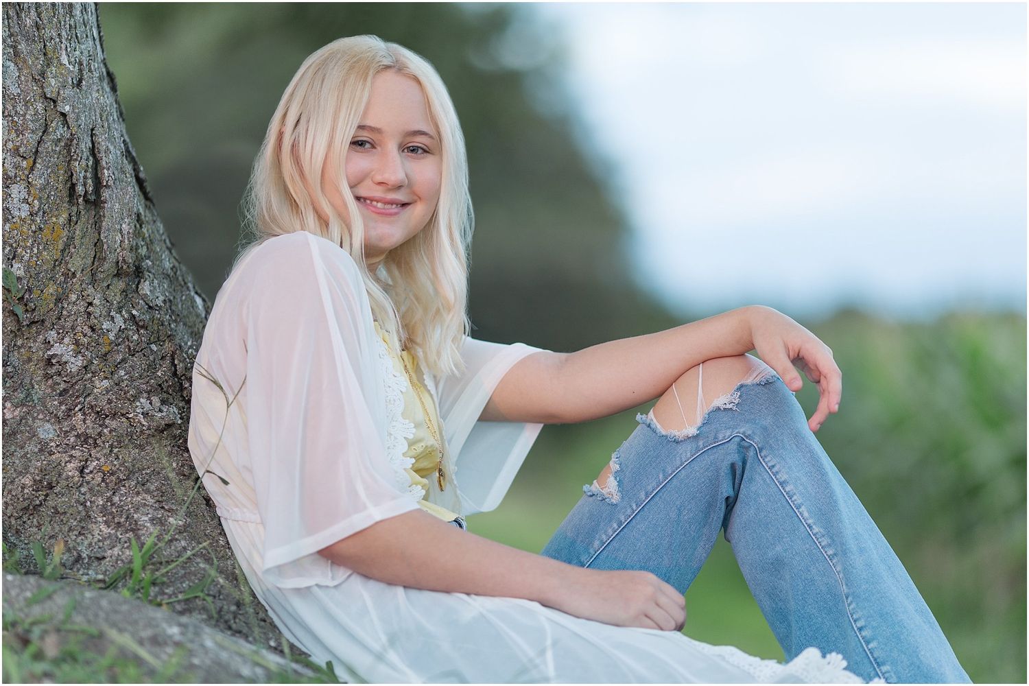 Senior girl leaning against a tree by a corn field