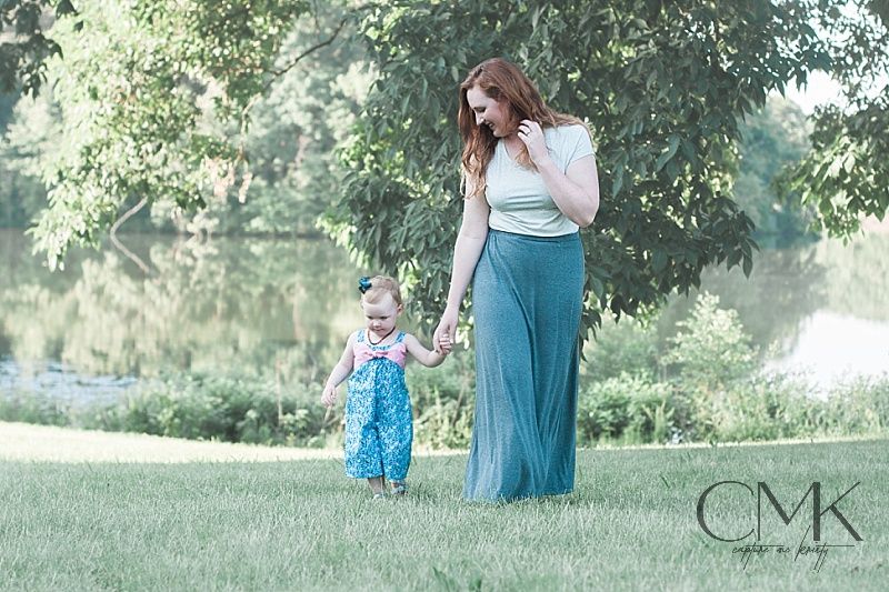 Parent and small child walking together on grassy lawn during golden hour outdoor photoshoot.