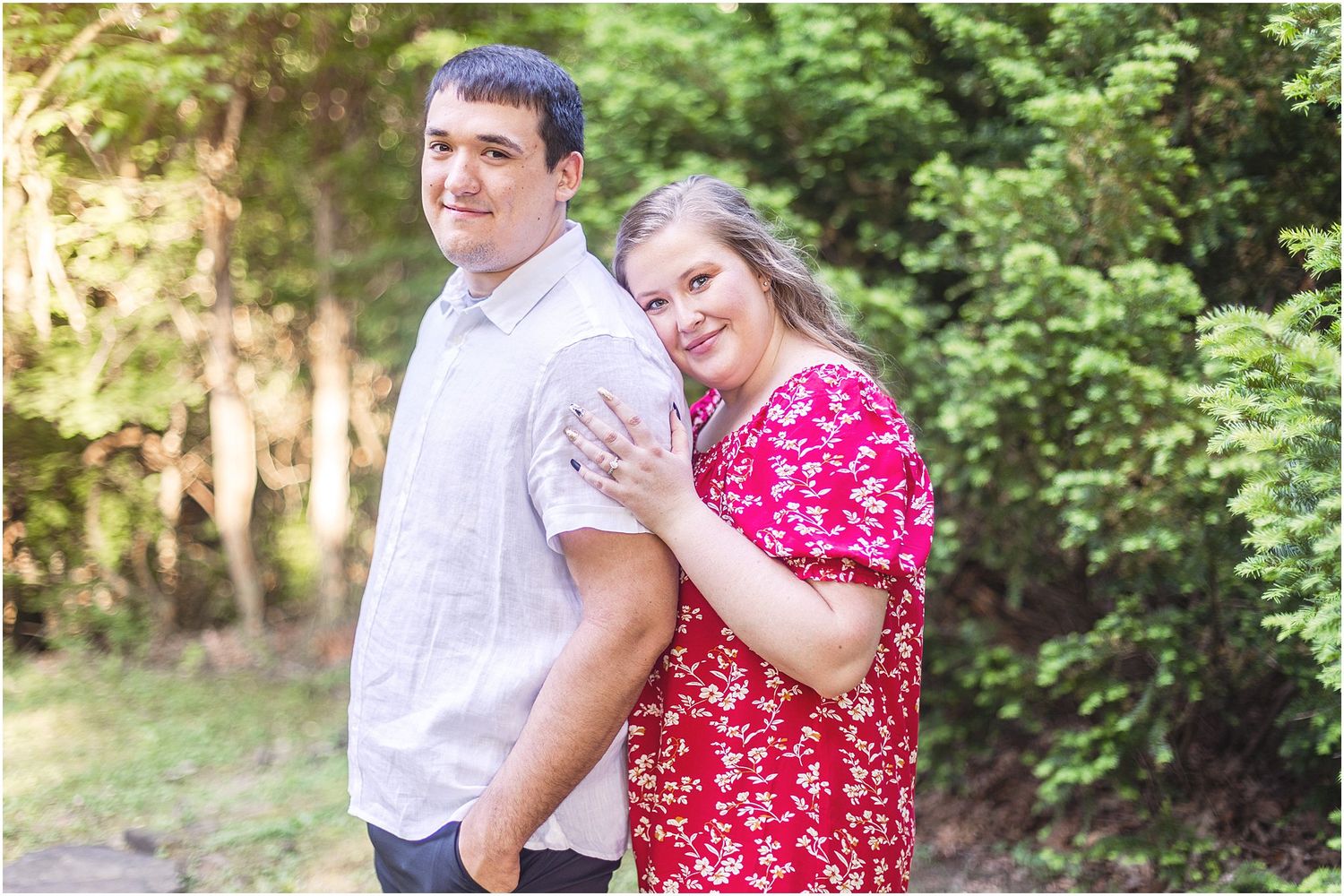Couple poses playfully in a garden setting wearing white and red floral outfits during a romantic photoshoot.