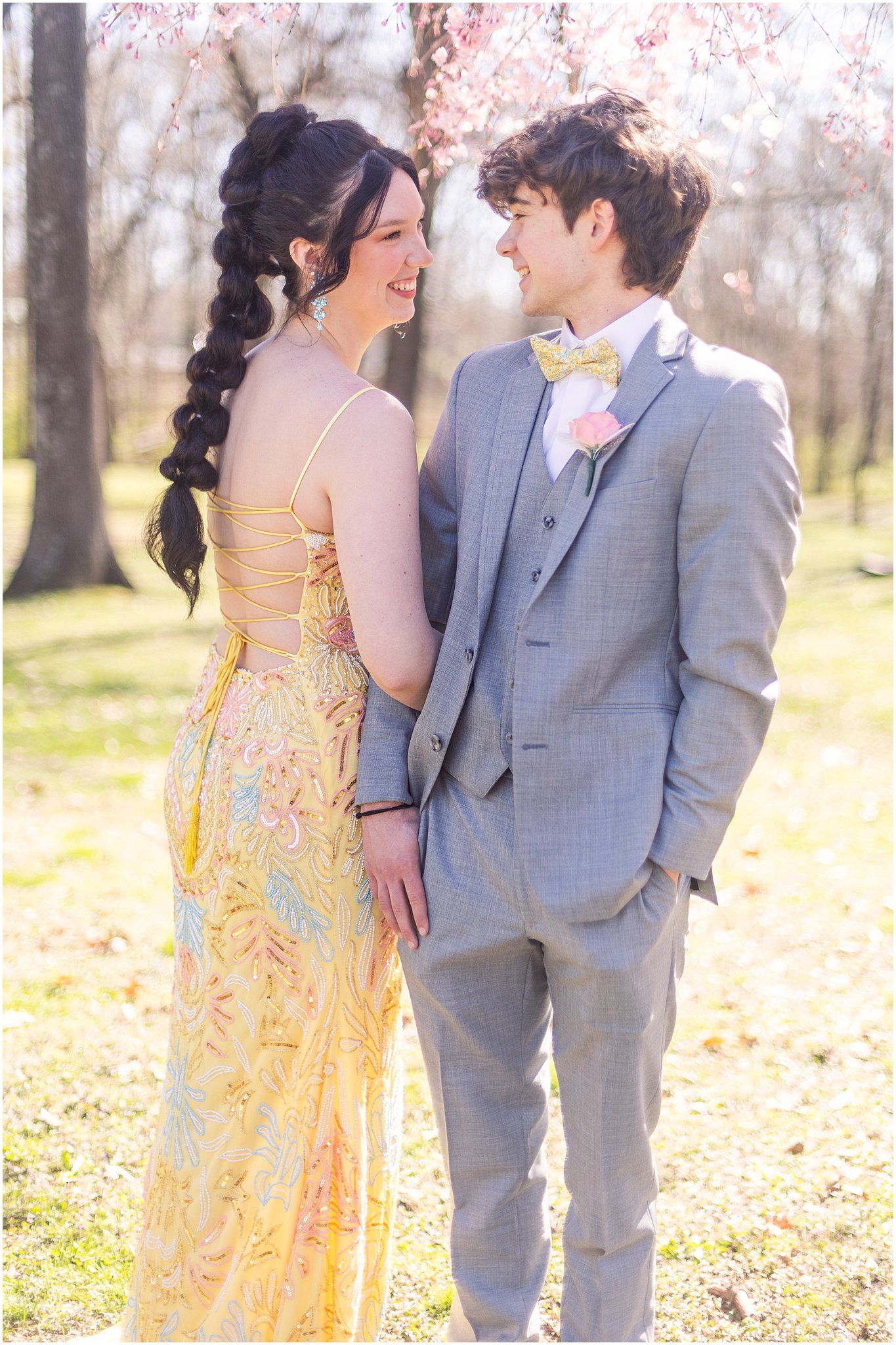 Couple sharing romantic moment in formal wear under blooming spring trees.