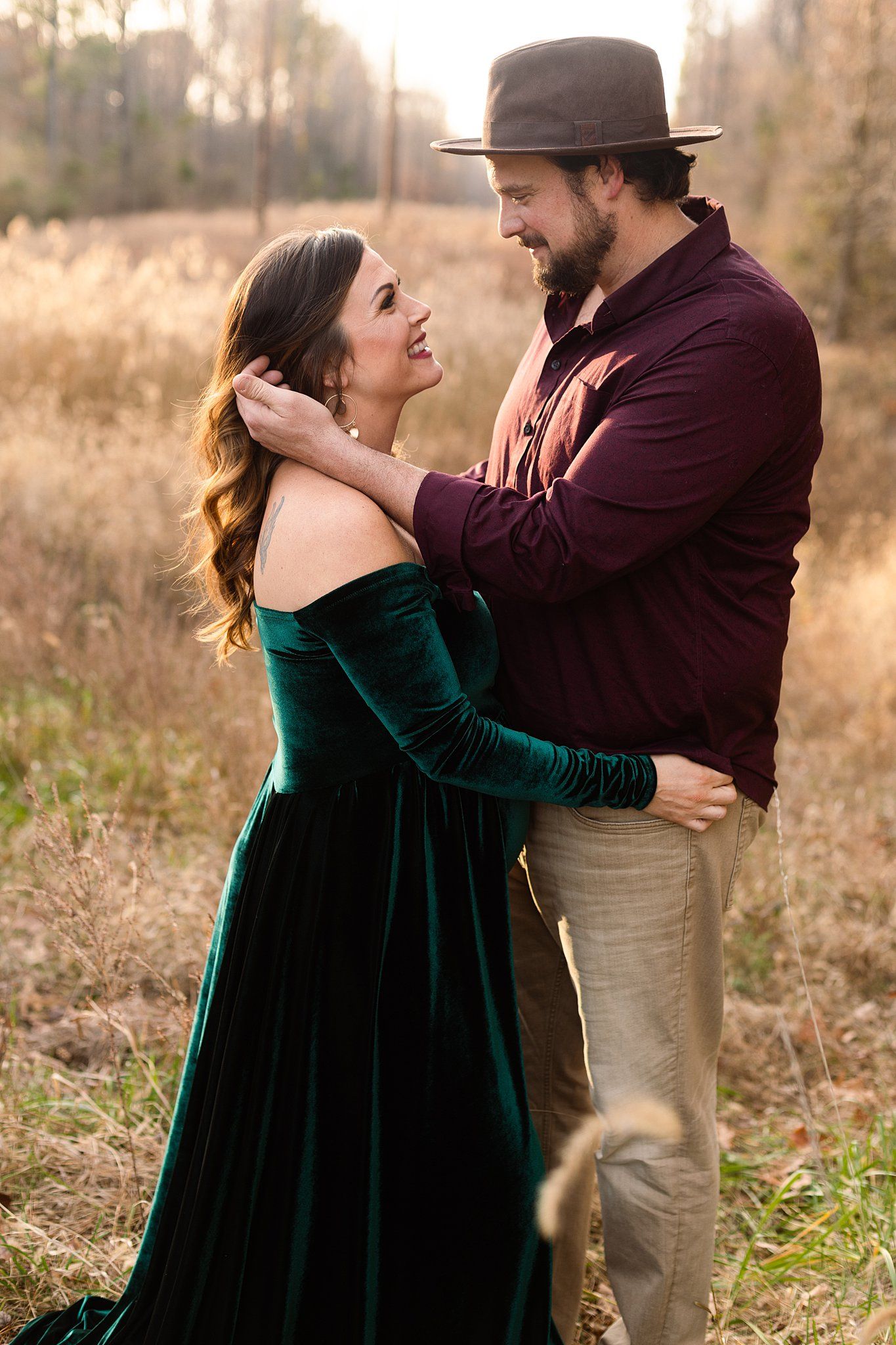 A romantic couple's portrait in a field with the woman wearing an elegant green velvet dress.