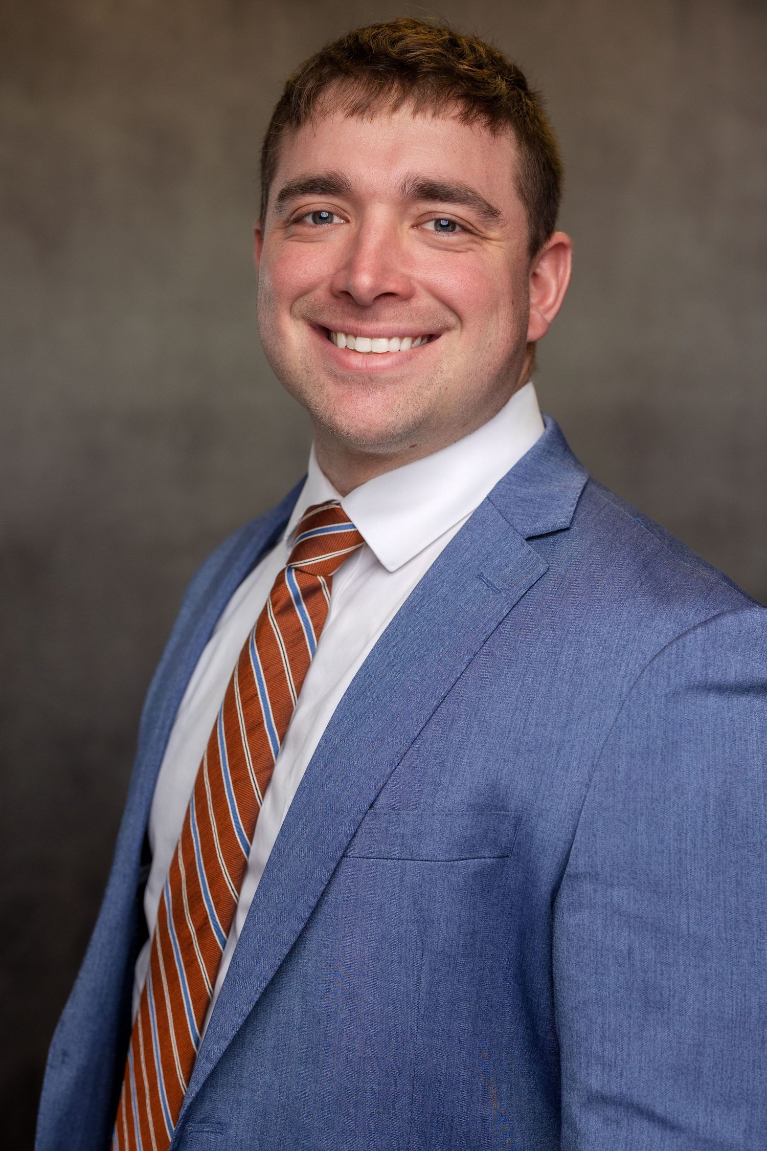 Professional headshots showing person in light blue suit and striped tie against gray background.