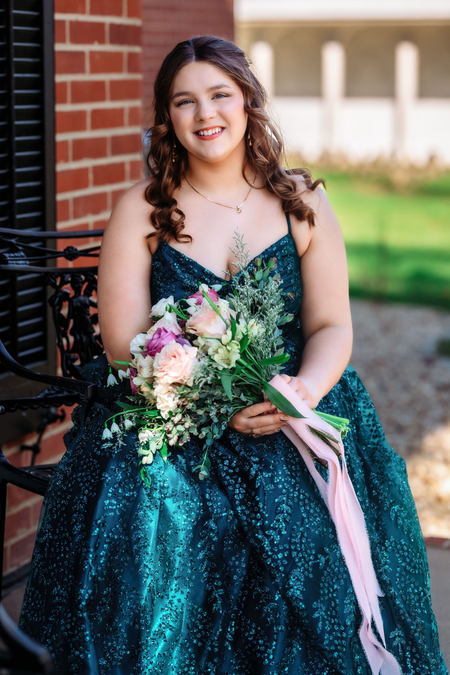 A person in a sparkly emerald green formal dress holds a pink and white floral bouquet.