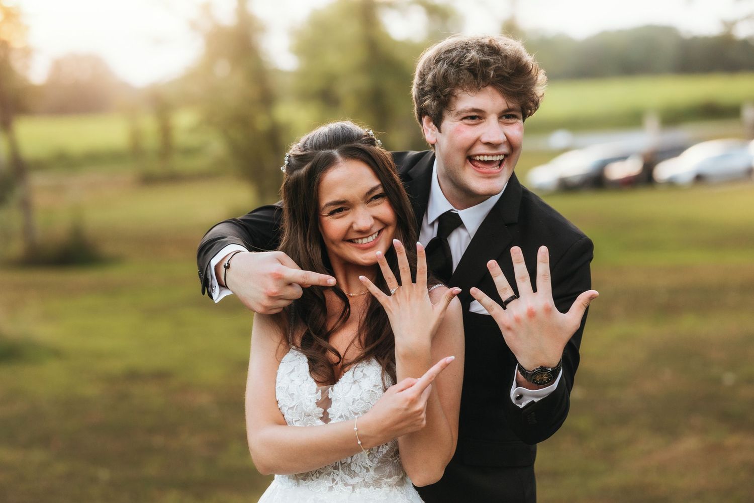 Playful wedding portrait of newlyweds showing their rings with joyful expressions.