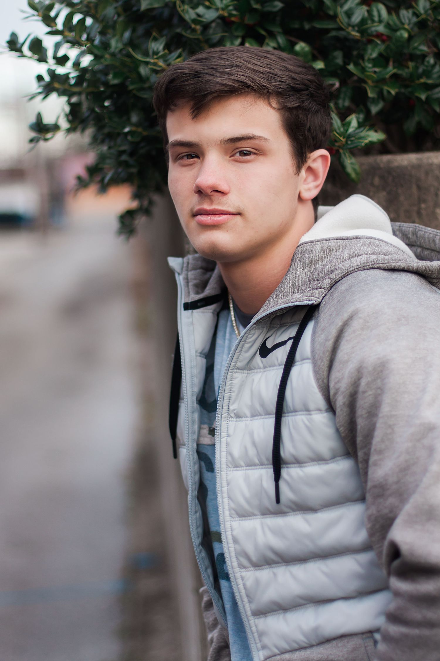 Person in gray puffer jacket and hoodie poses against blurred outdoor background.