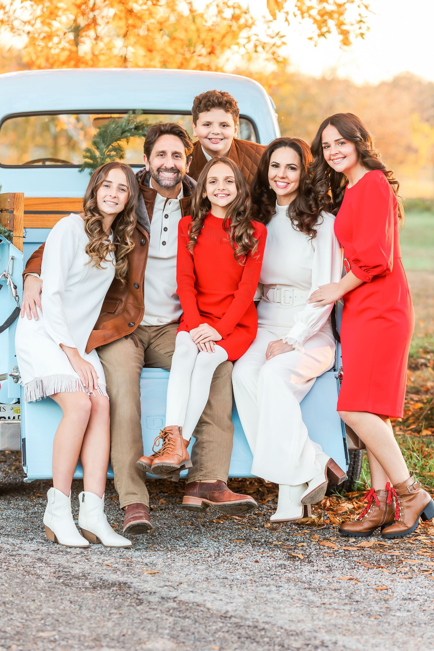 People sit together by a vintage blue truck showing their coordinated red and white outfits.