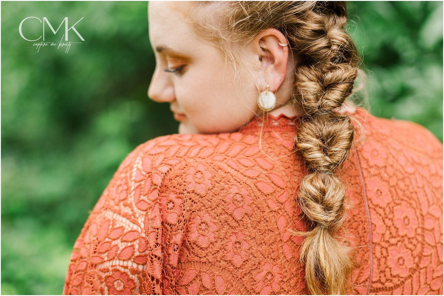 Close-up of braided hairstyle and coral lace dress detail against green background.
