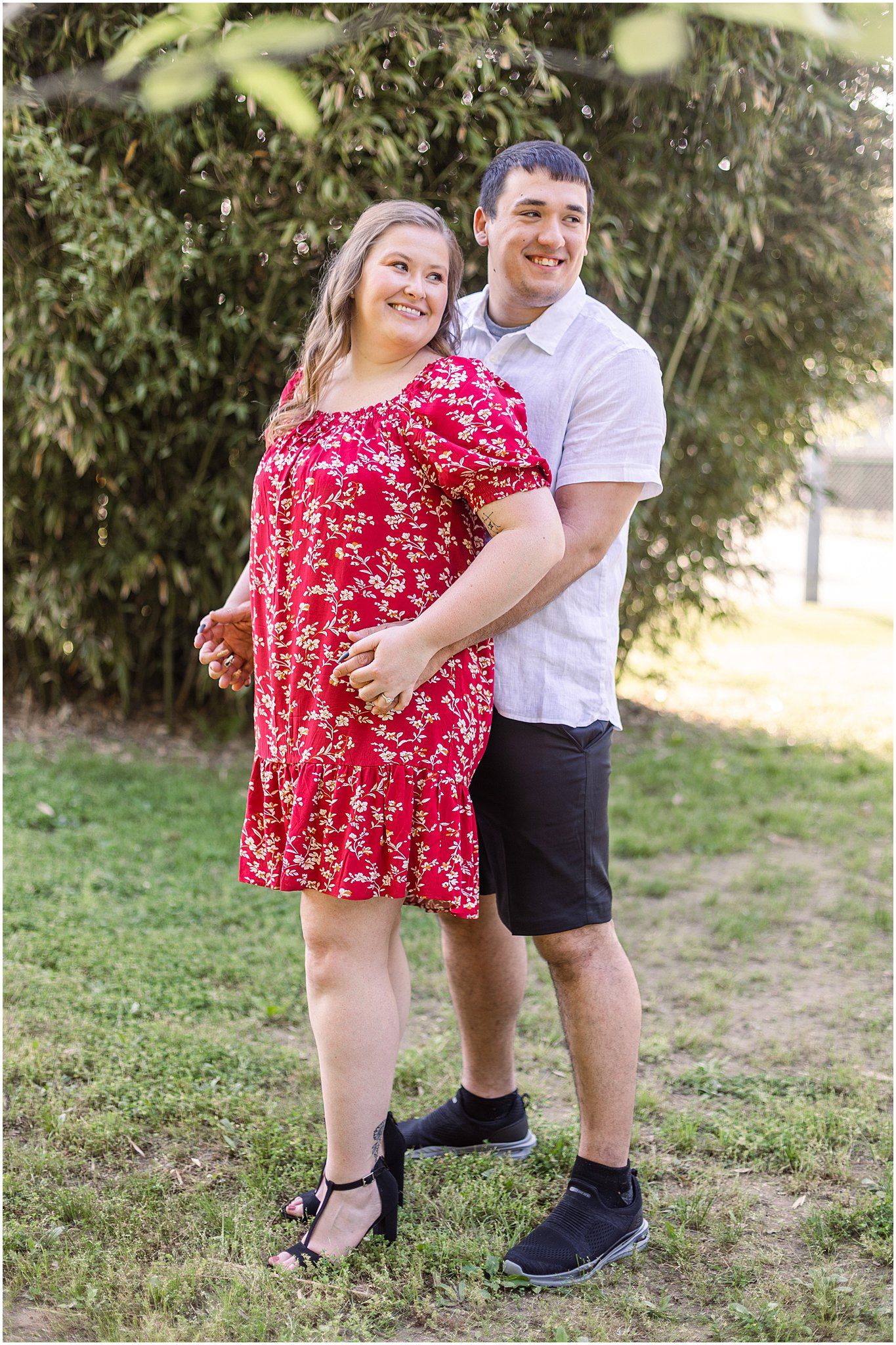 Outdoor portrait of couple in red floral dress and white shirt against natural background.