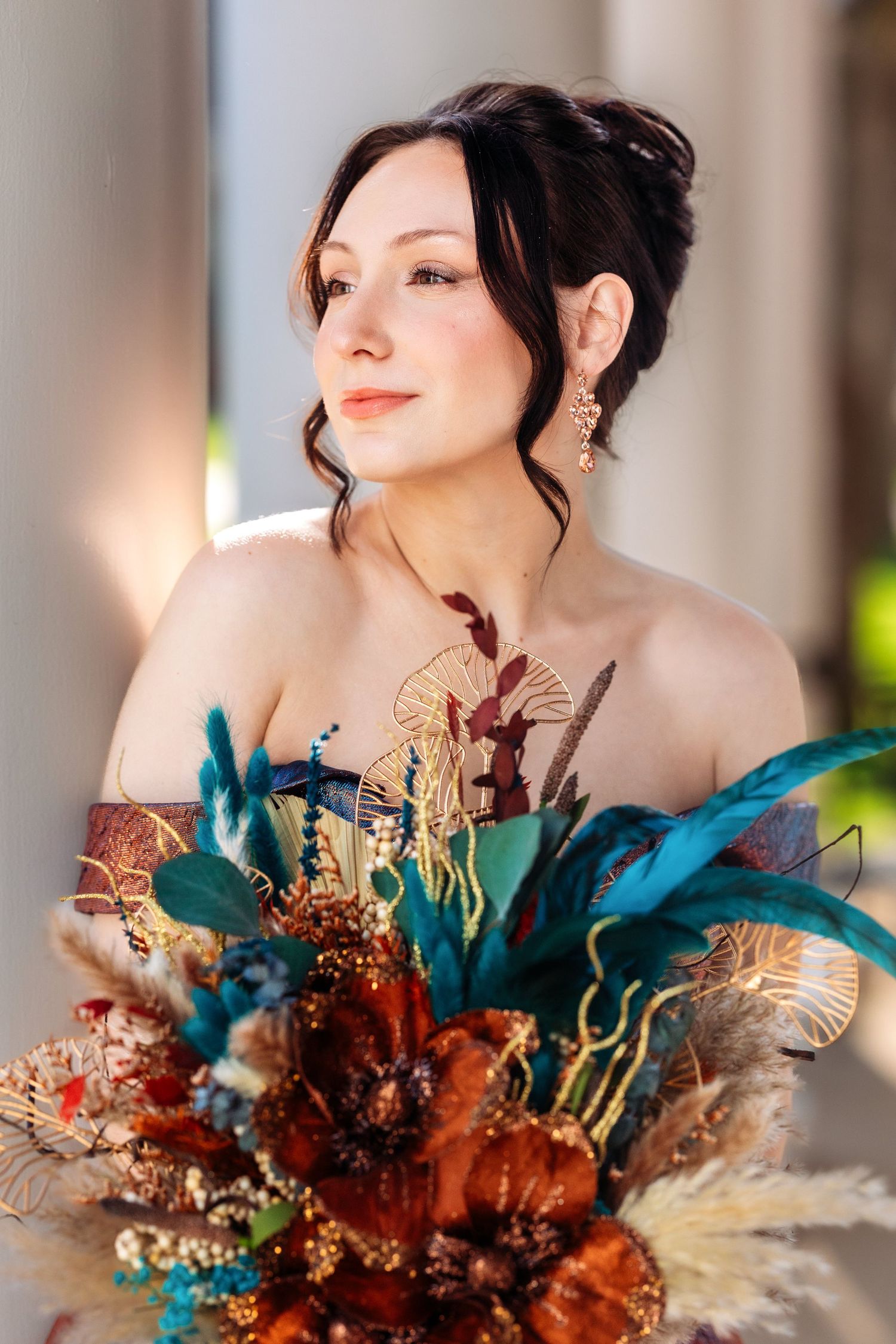 Elegant portrait with a dramatic autumn-colored bouquet featuring blue and copper feathers.