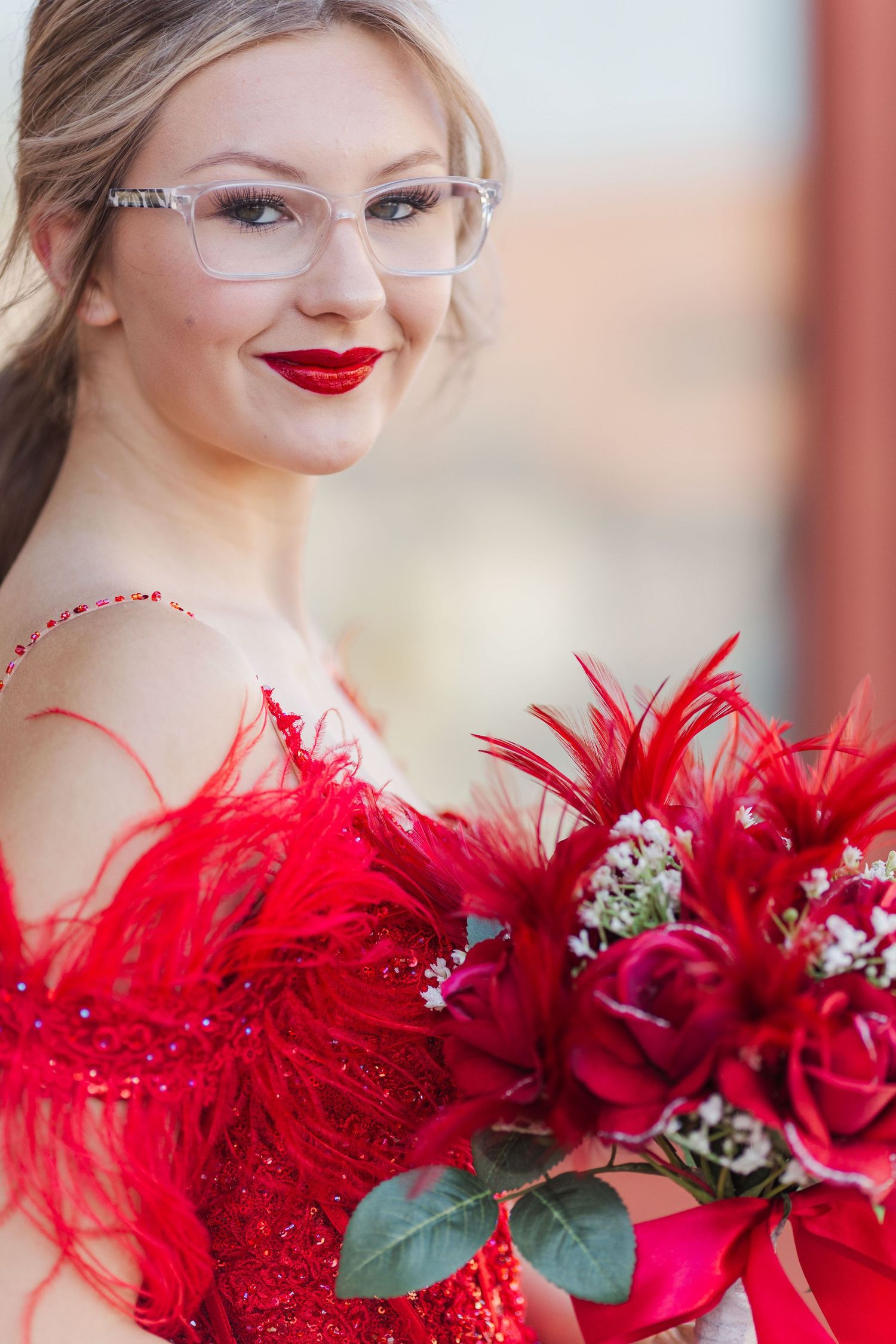 A red feathered bouquet with roses and greenery complements a formal dress.