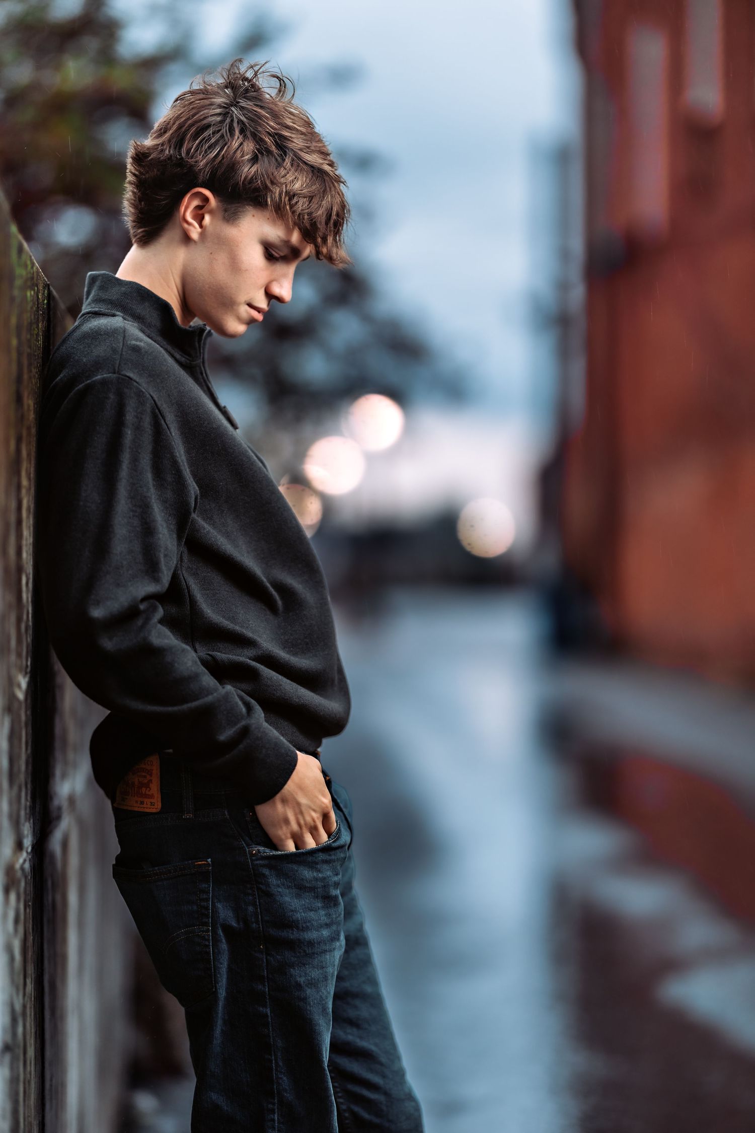 Person in dark clothing leaning against wall in moody evening lighting.