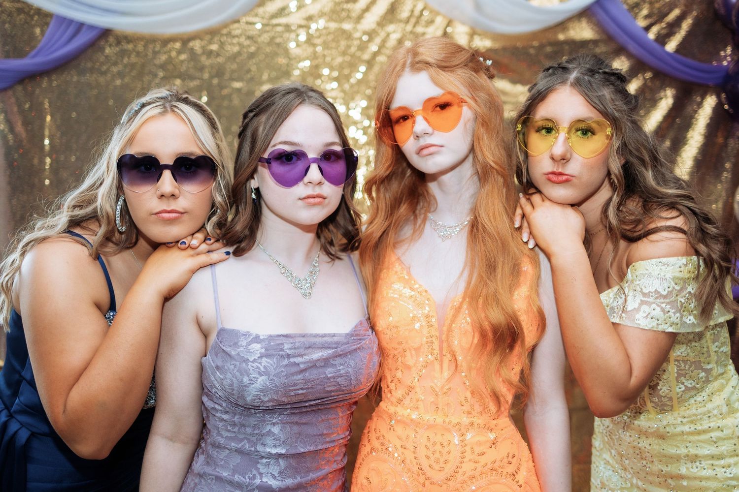 Party guests wearing colorful sunglasses pose together at a celebration.