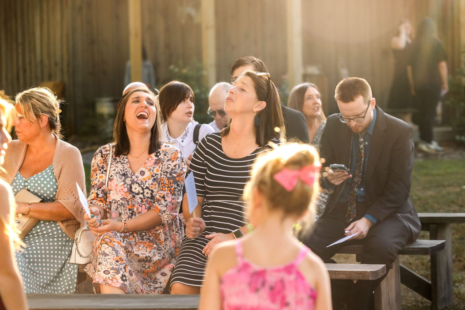 Wedding guests laugh and smile during an outdoor celebration.