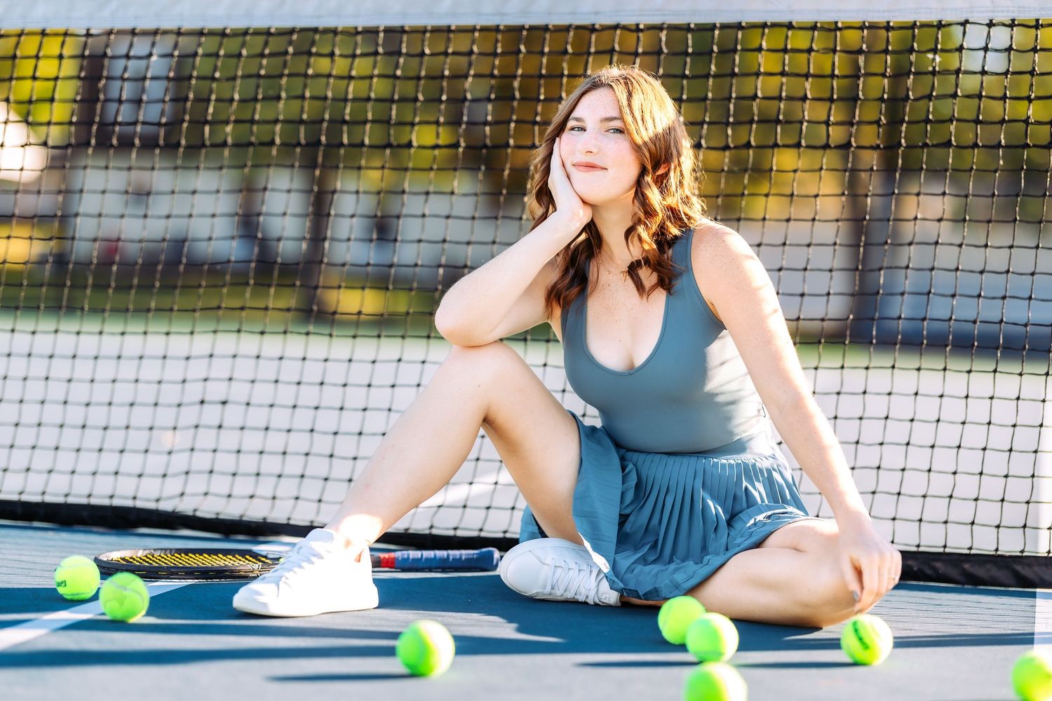 Athletic fashion shoot at a tennis court with teal activewear and yellow tennis balls.