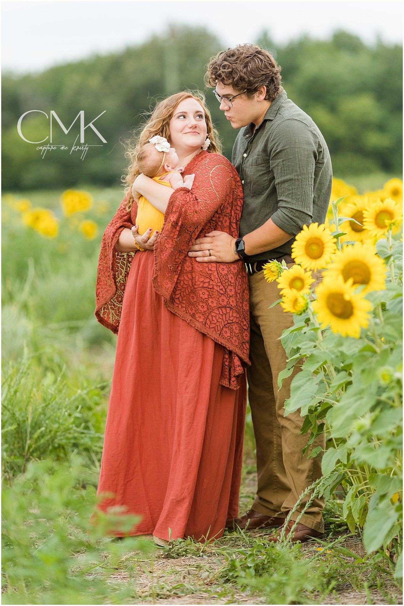 Family standing together in sunflower field wearing coordinated autumn colors.