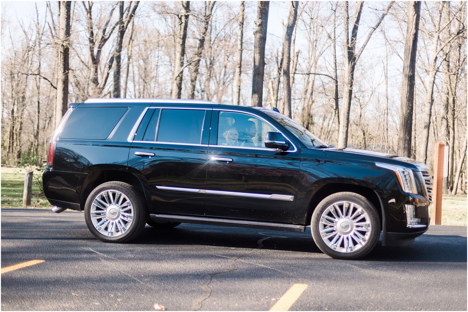 Black Cadillac Escalade SUV parked on asphalt with bare trees in background.