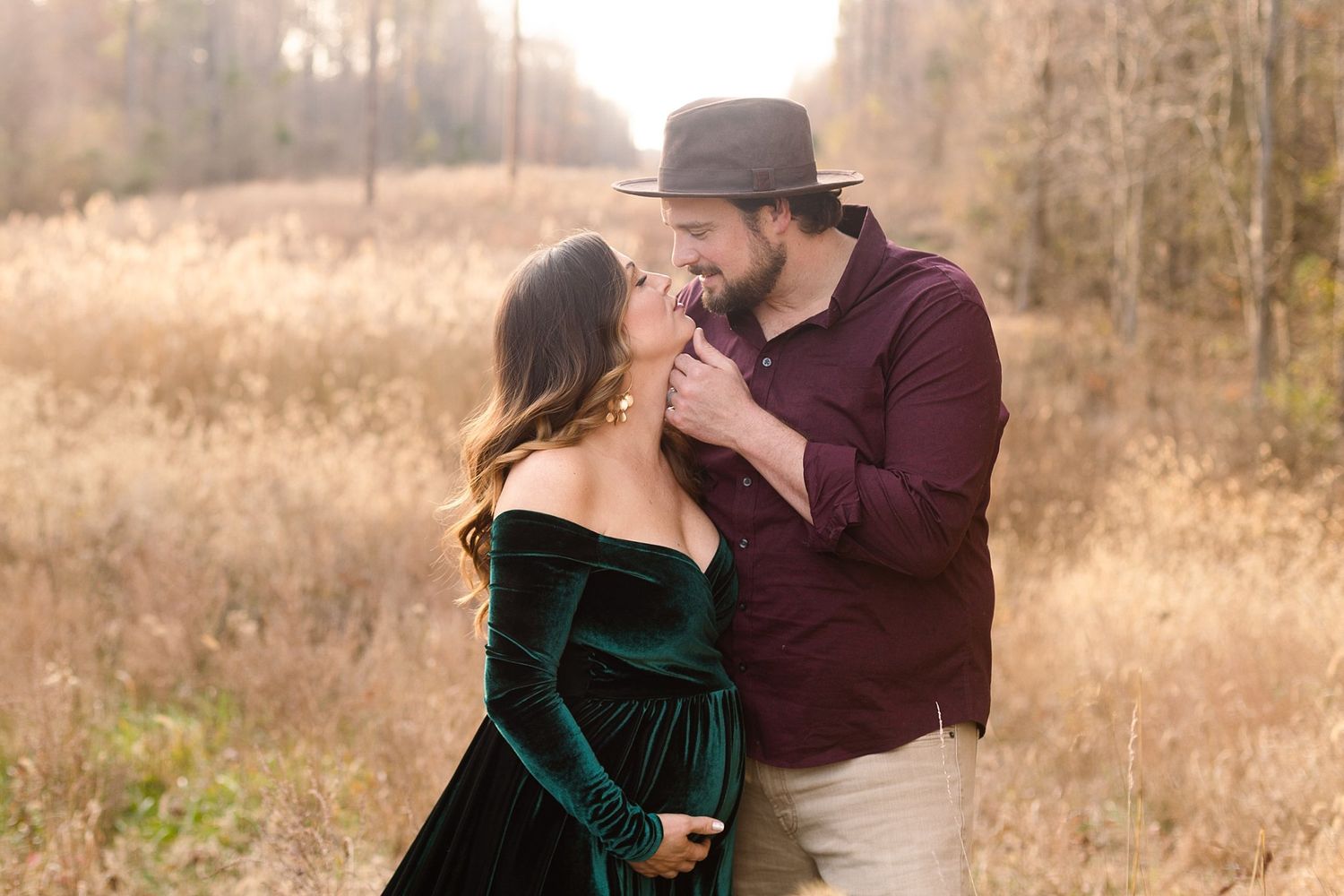Intimate moment captured between couple in autumn field wearing velvet dress and burgundy shirt.