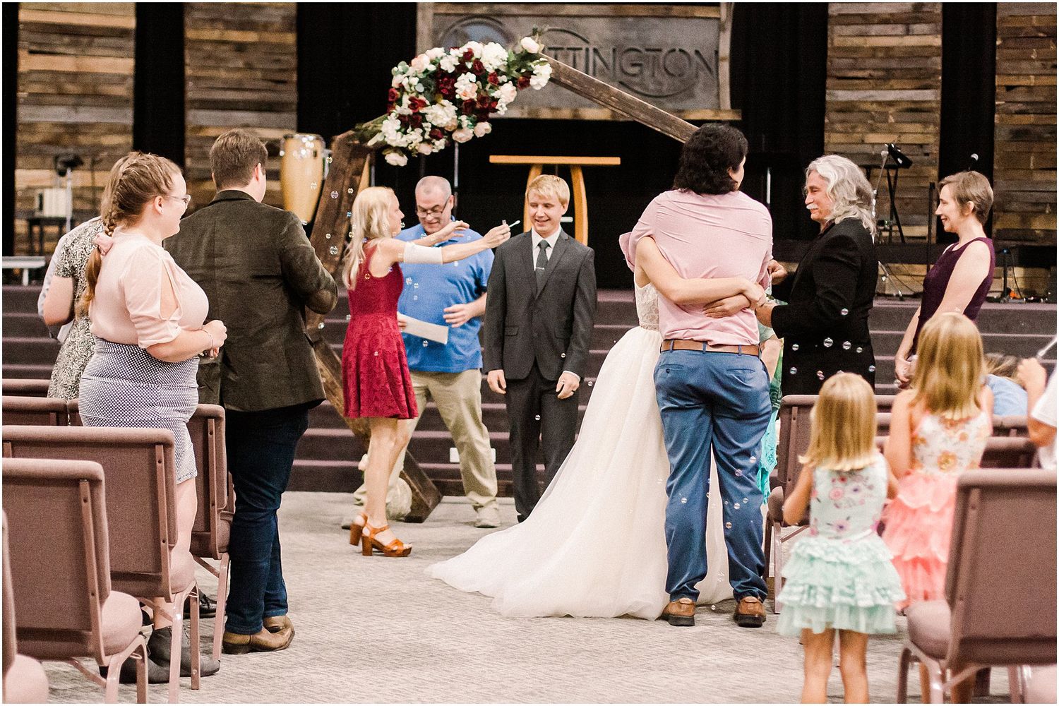 Wedding guests gather around the happy couple after the ceremony under a floral decorated arch.