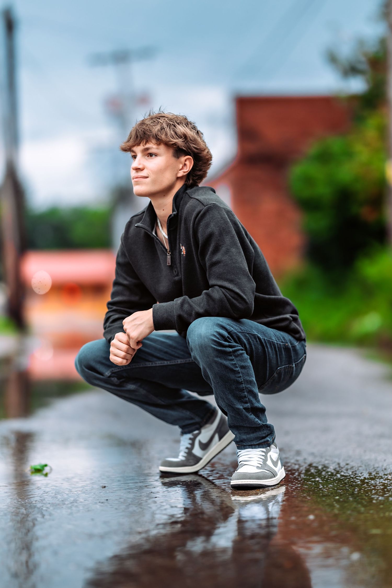 Action sequence of a person performing a skateboarding trick over a puddle on a rainy day near brick buildings.