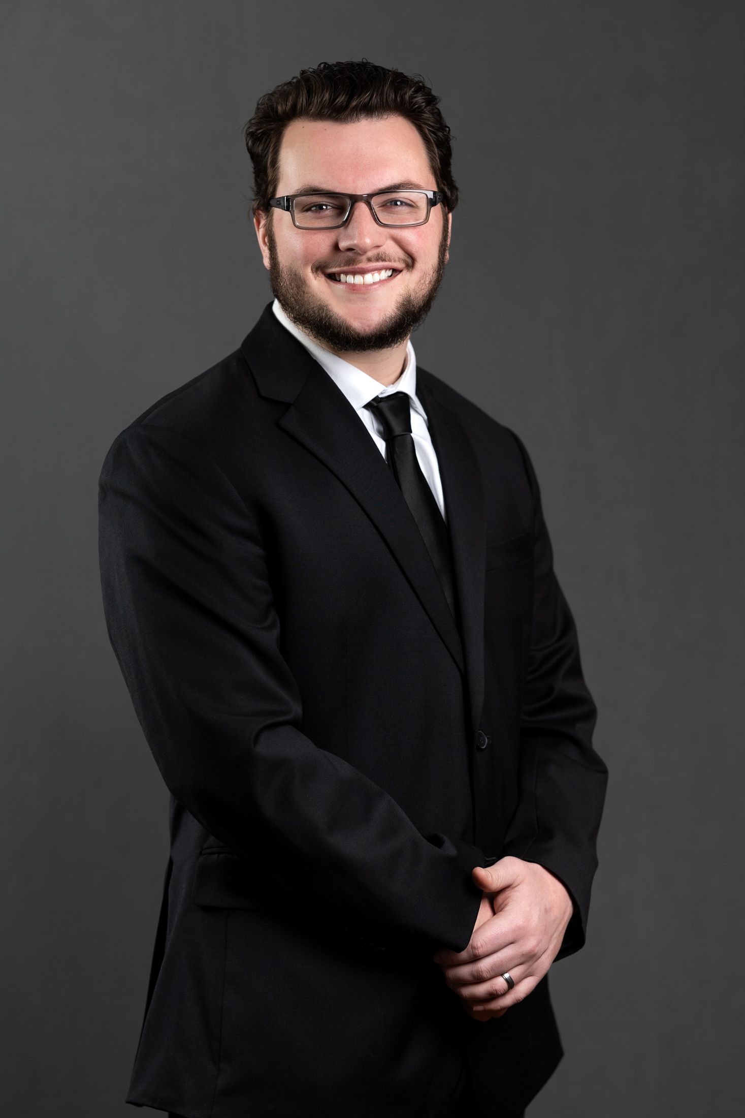 Professional headshots of man in black suit and tie against dark background.