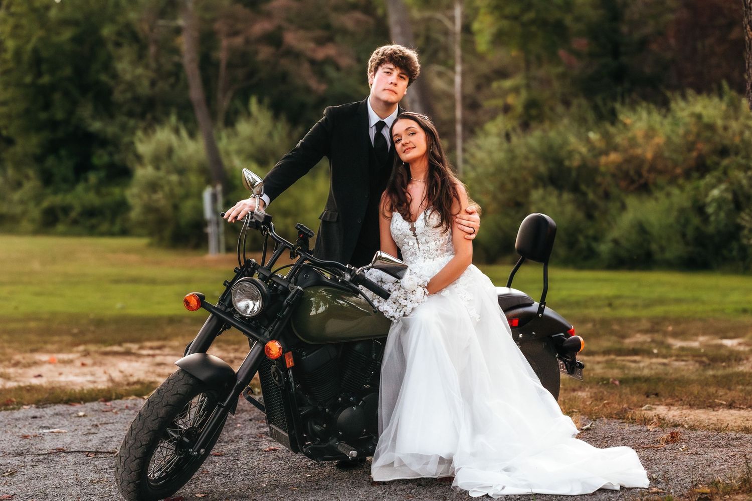 Newlyweds pose together on a motorcycle in formal wedding attire.