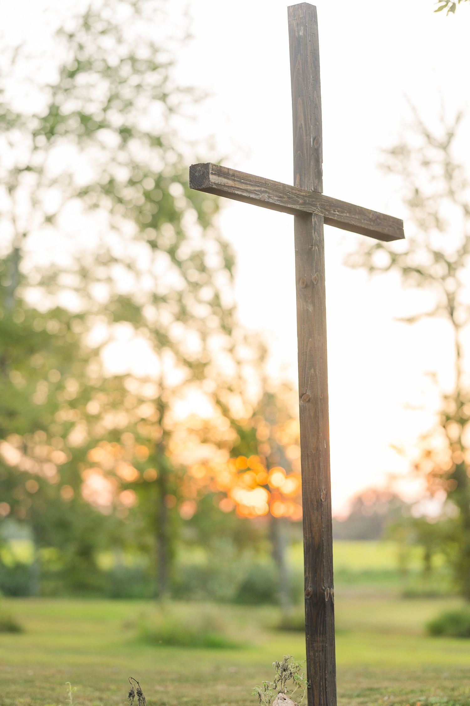 Wooden cross silhouetted against a sunset sky in a peaceful outdoor setting.