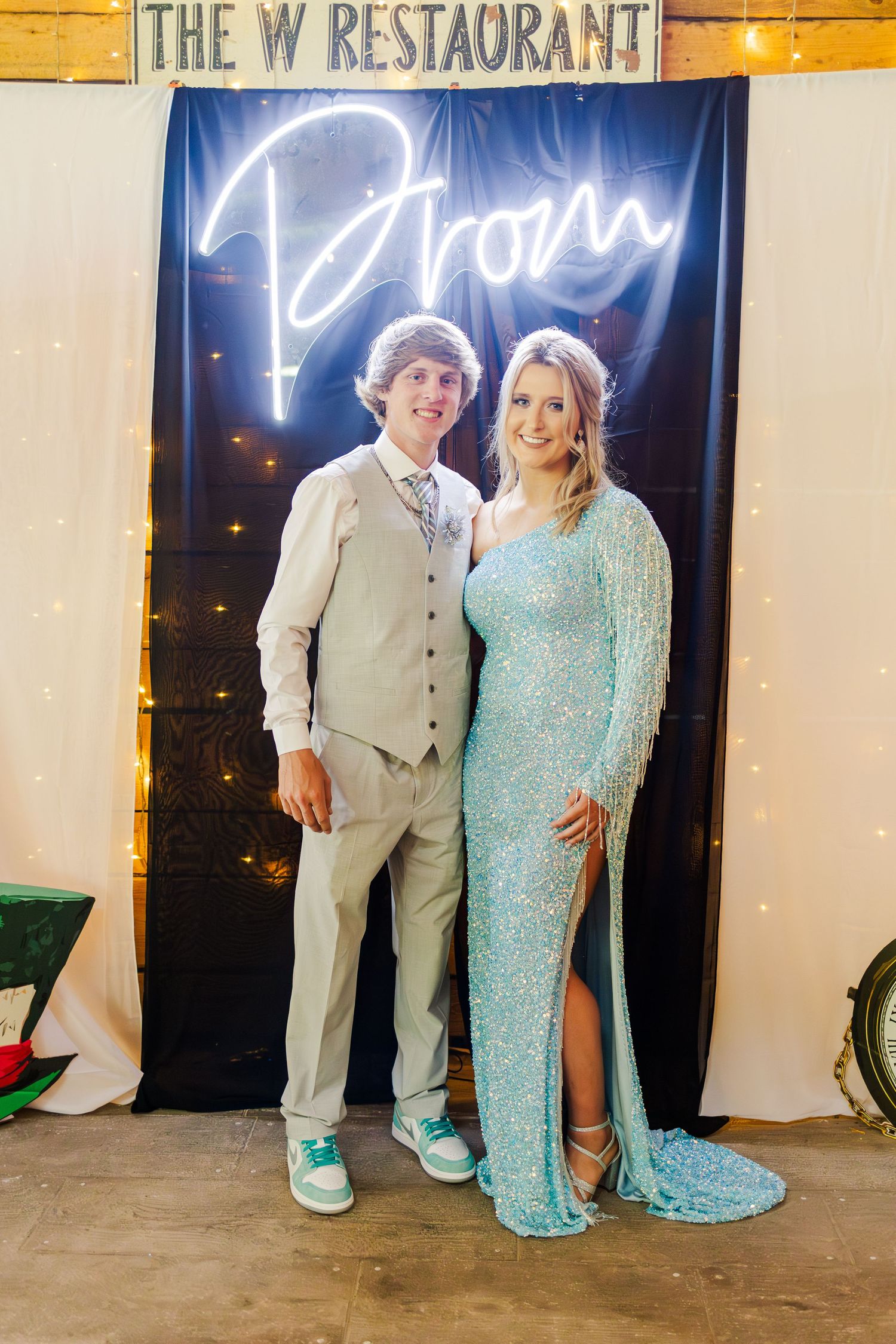 Couples posing in formal attire against a backdrop with 'The W Restaurant' signage and neon lights.