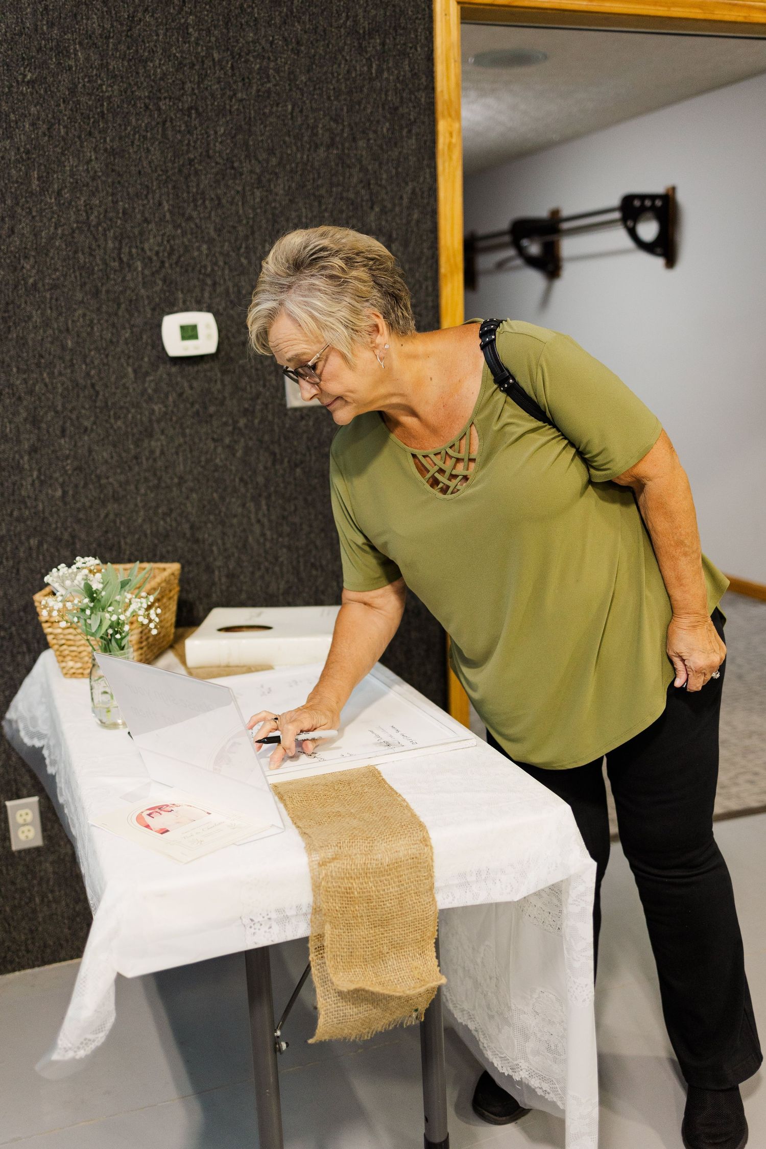 Person in olive green shirt leaning over a white tablecloth covered surface.