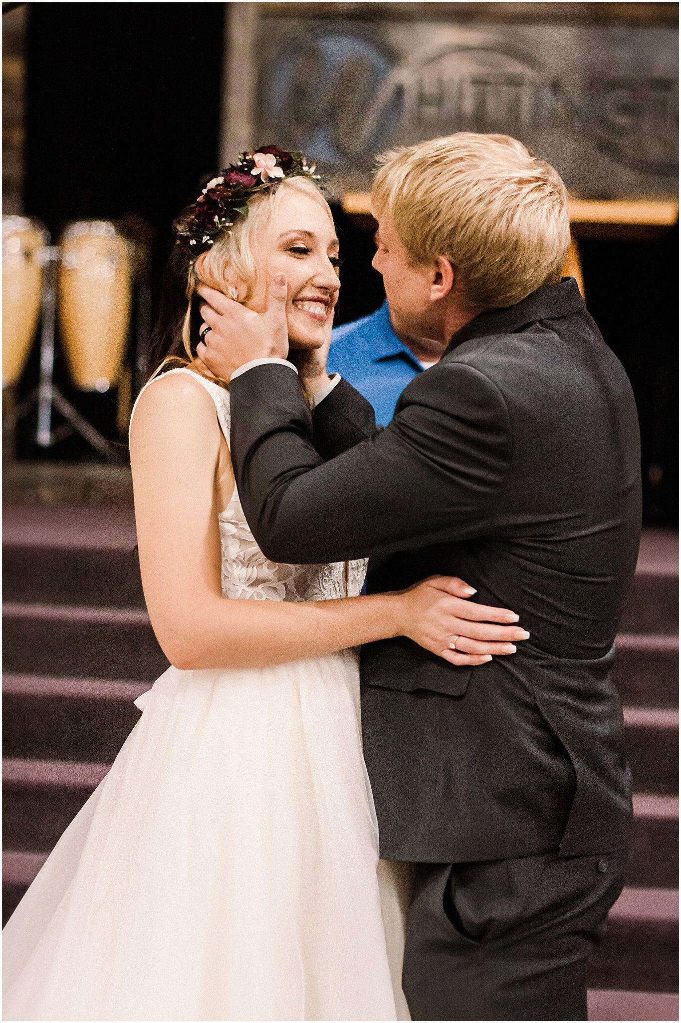 A tender moment between newlyweds during their first dance in a rustic venue with warm lighting.