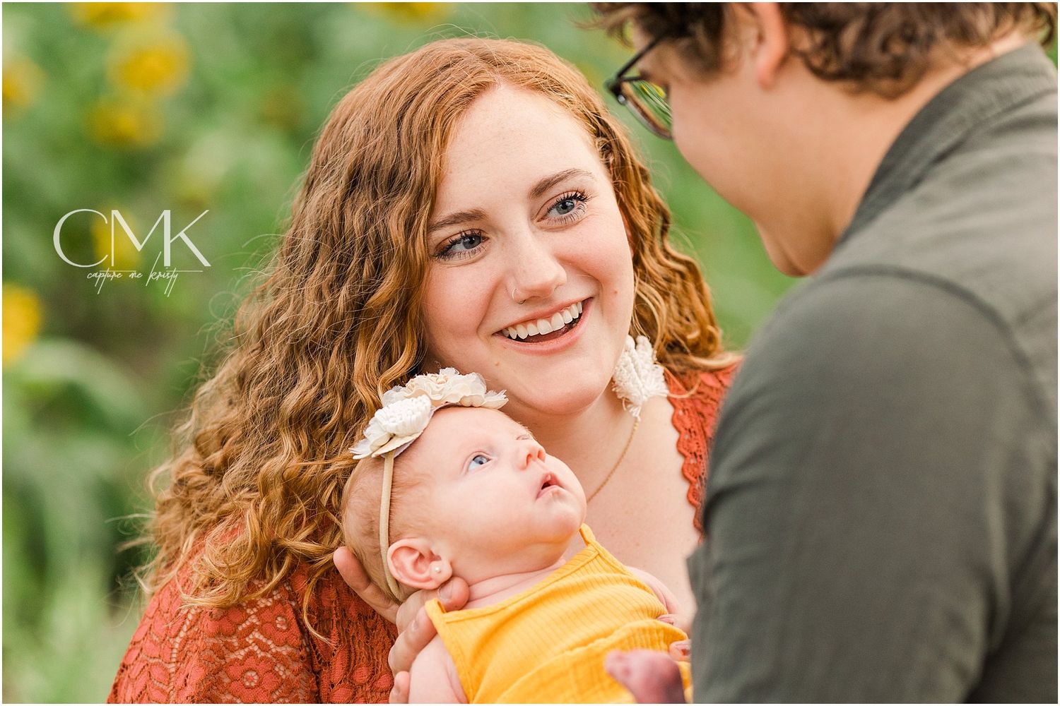 Candid family photo with baby in yellow outfit amid blooming flowers.
