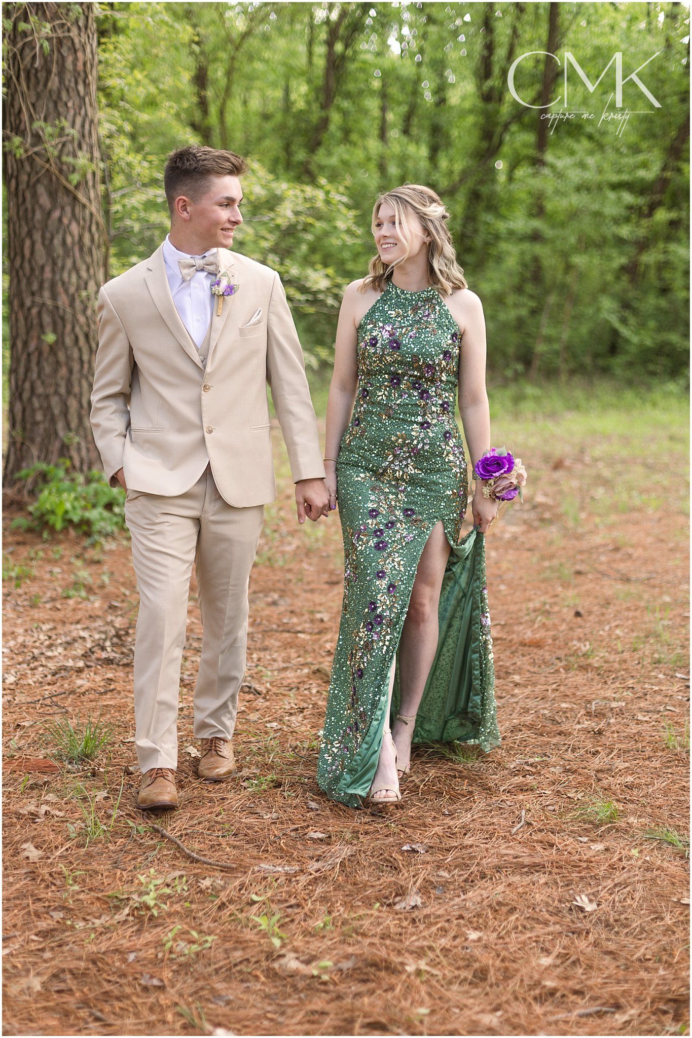 Formal couple strolling along a pine needle covered forest path.
