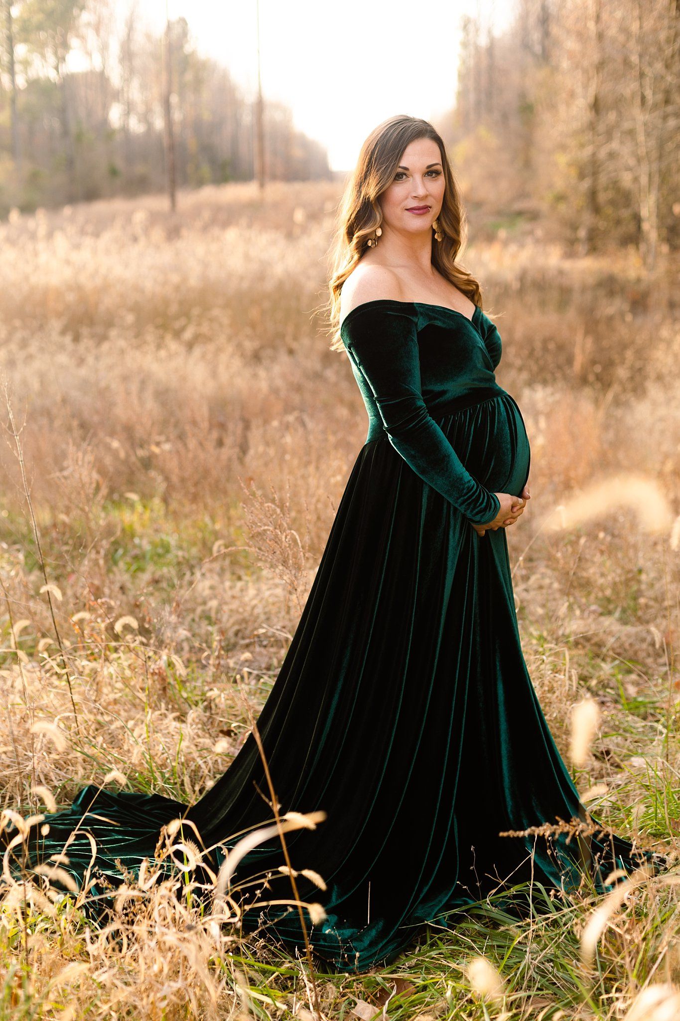 Elegant maternity photo with woman in off-shoulder emerald velvet gown in golden field.