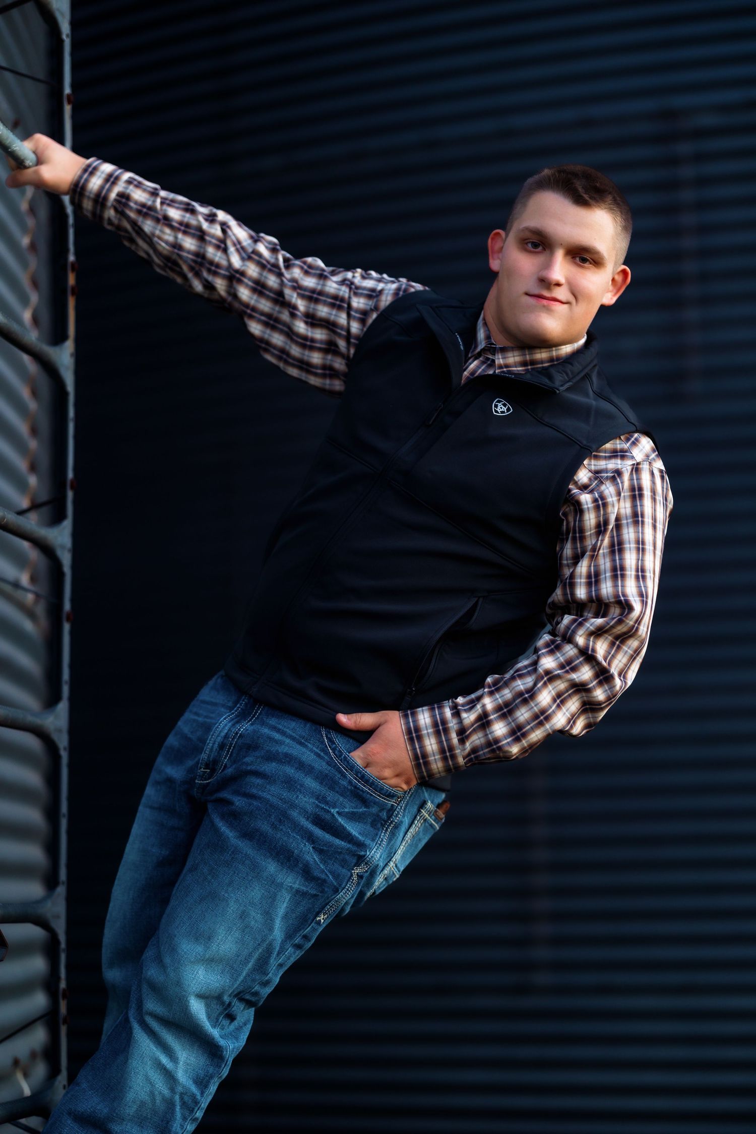 Person in casual attire posing against dark industrial wall.