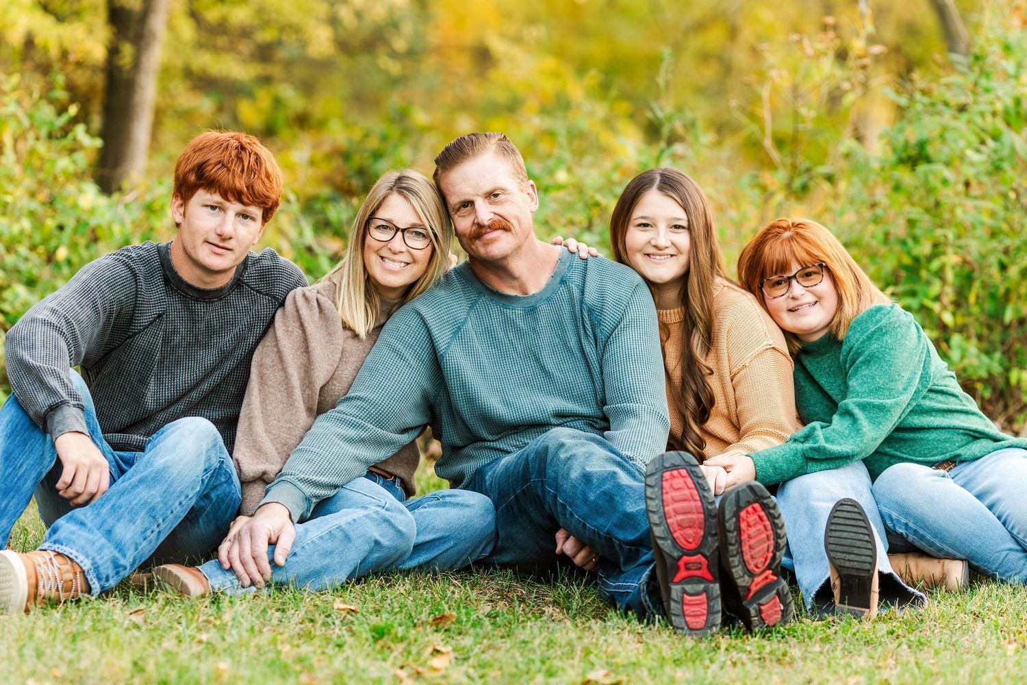 A group lounges casually in autumn grass wearing coordinated blue and teal outfits during an outdoor photo session.