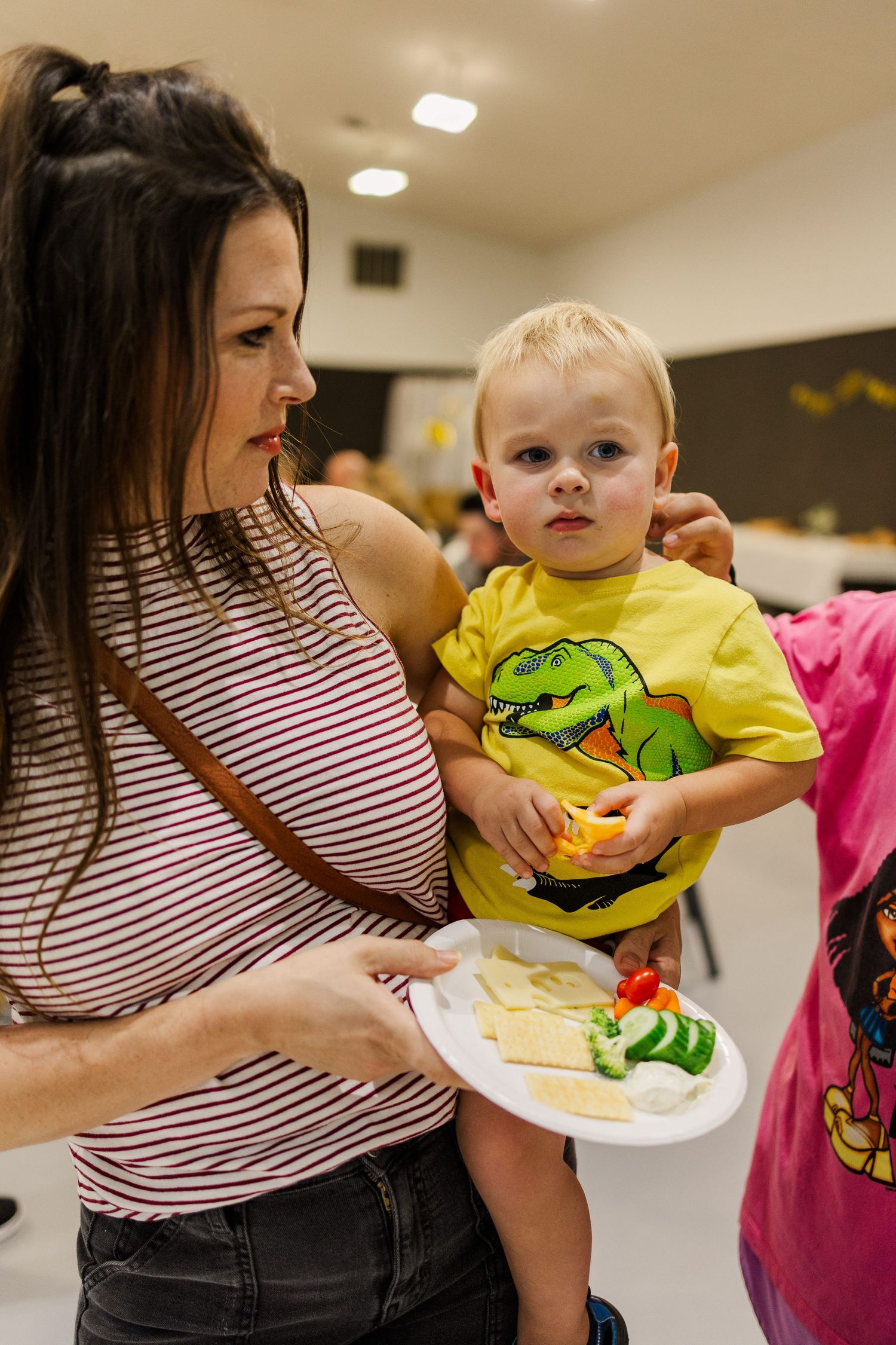 A small child in a yellow shirt being held while reaching for food at a buffet table.