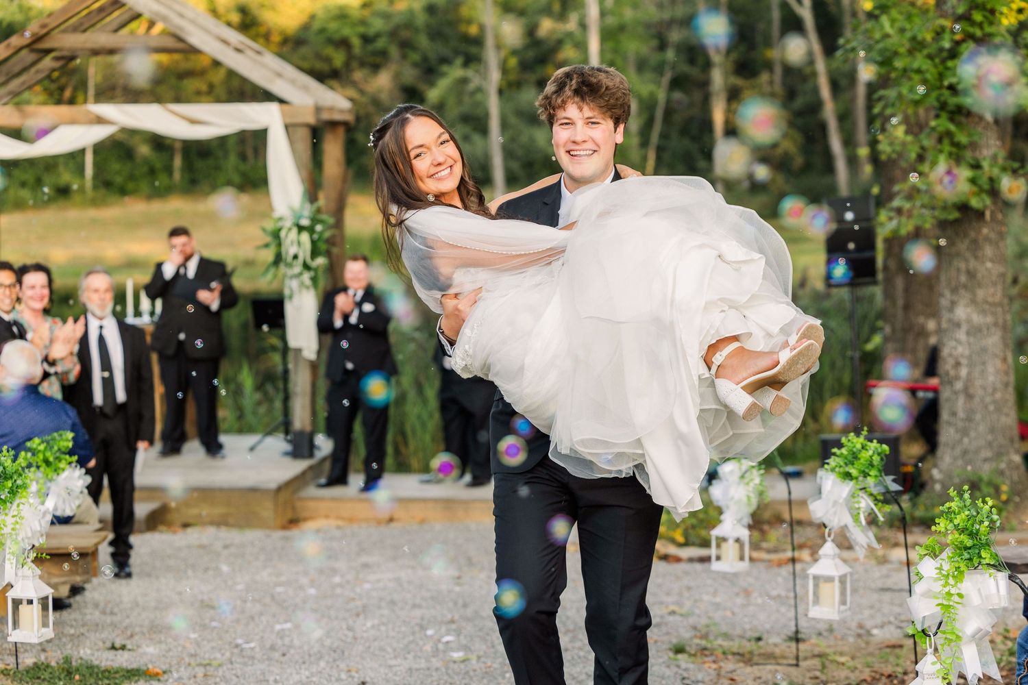 A joyful moment as the groom carries his bride across a decorated outdoor pathway.