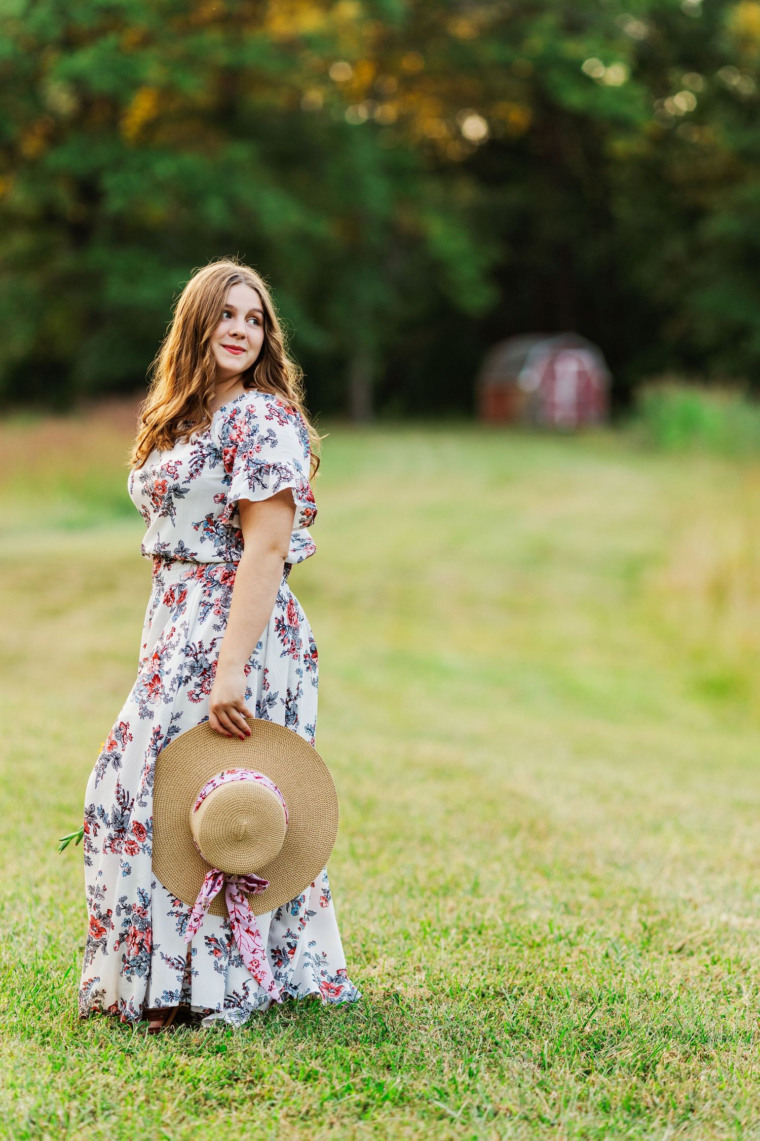 A flowing floral maxi dress and straw hat create a romantic countryside scene.