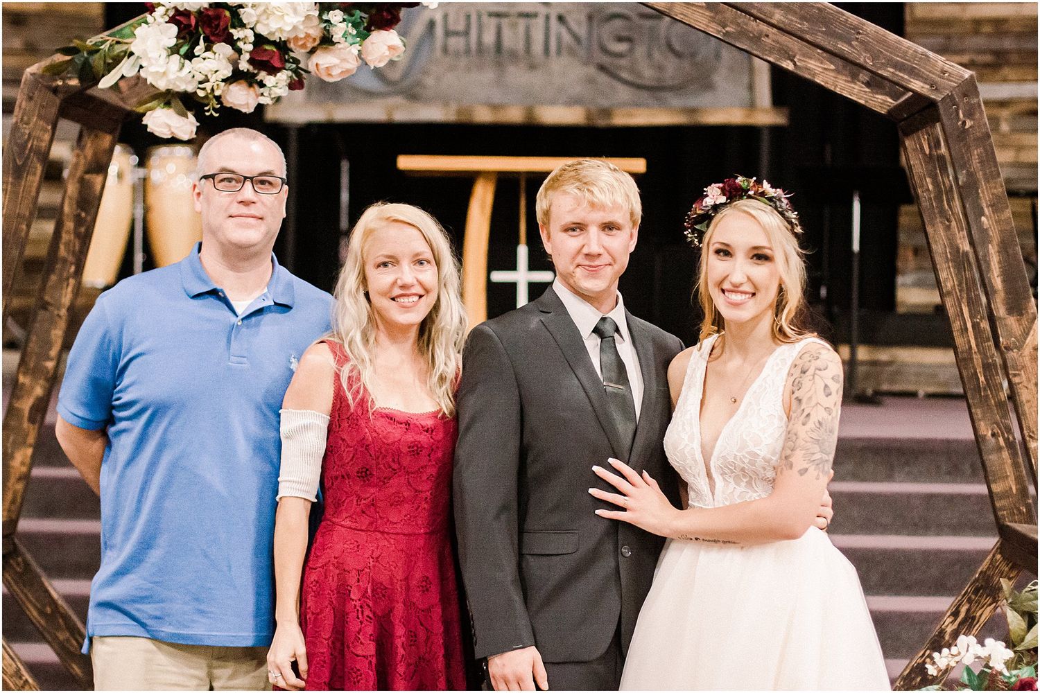 Four people pose together at a rustic wedding venue with floral decorations.