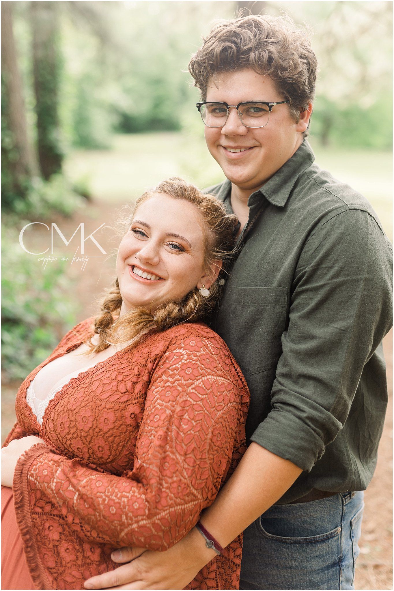 Romantic couples maternity portrait outdoors among green trees.