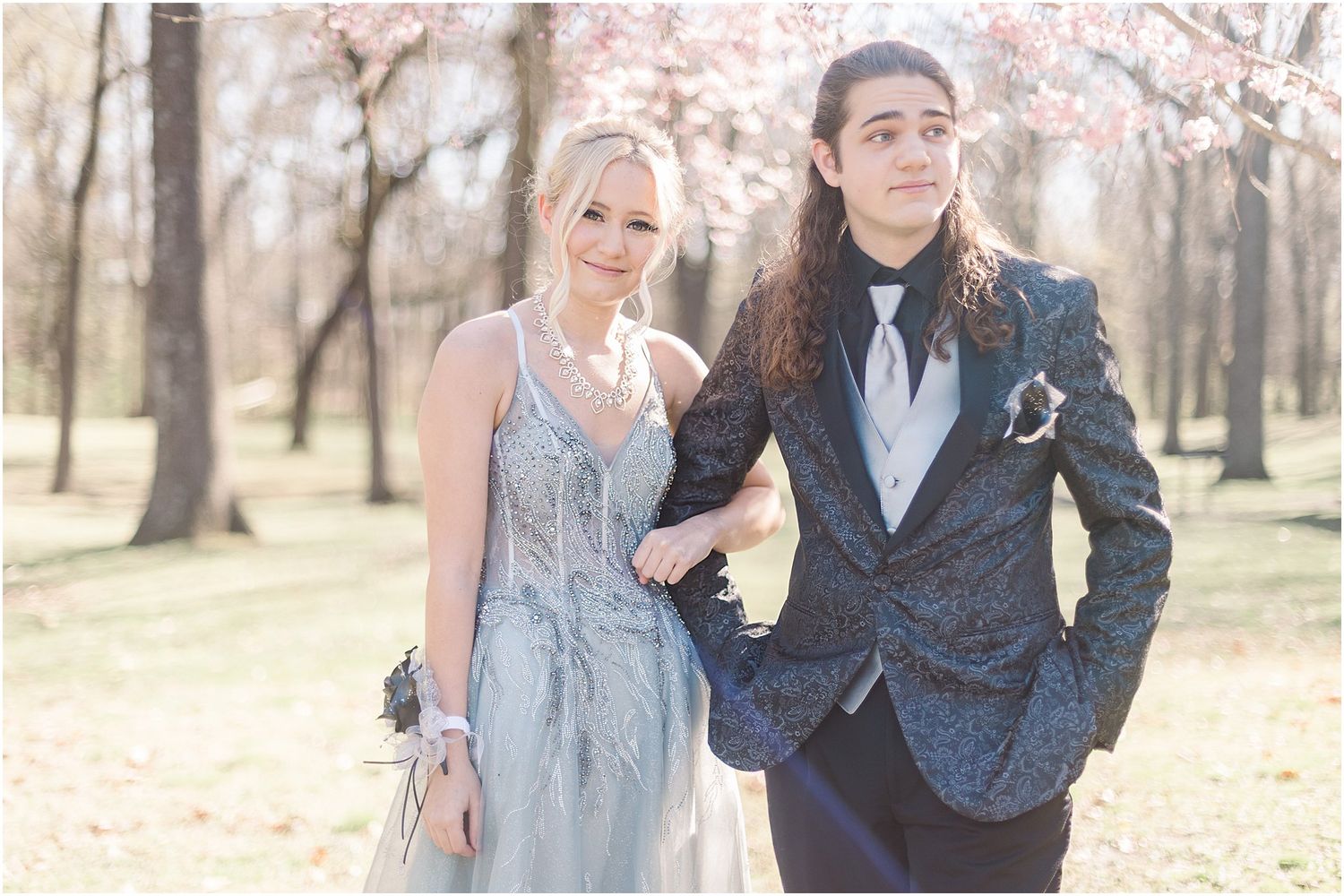 A couple in evening wear pose together in a spring outdoor setting.