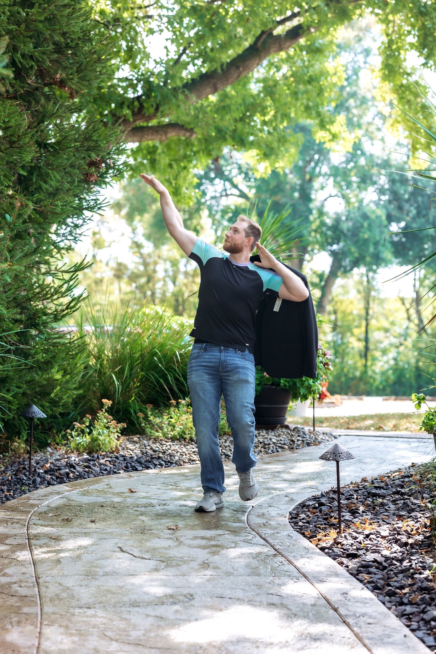 Guy practicing dance moves on a garden pathway surrounded by lush greenery.