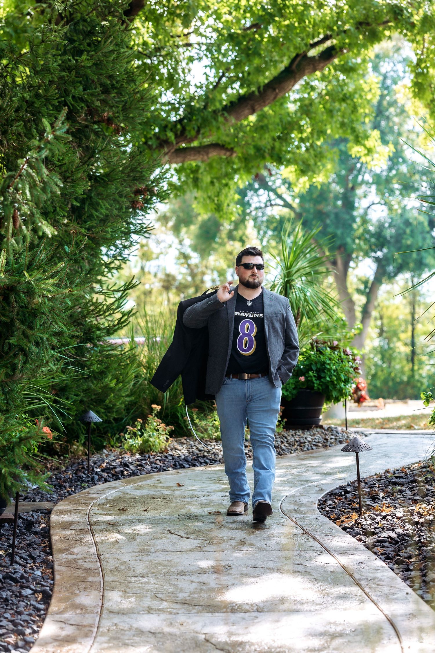 Person in casual attire walking along curved garden path with sunlit trees.