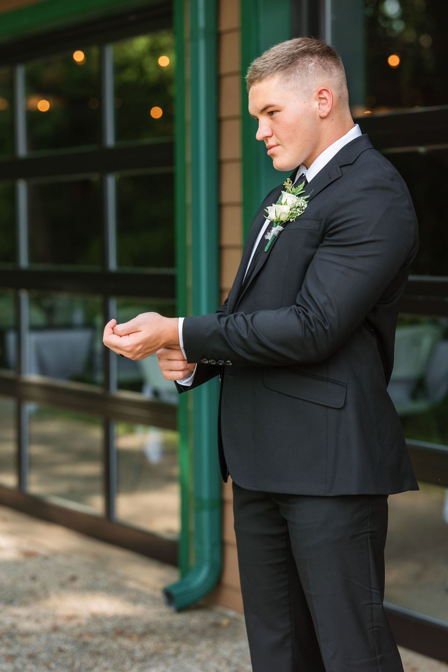 Groom in black tuxedo adjusting his cufflinks outdoors.