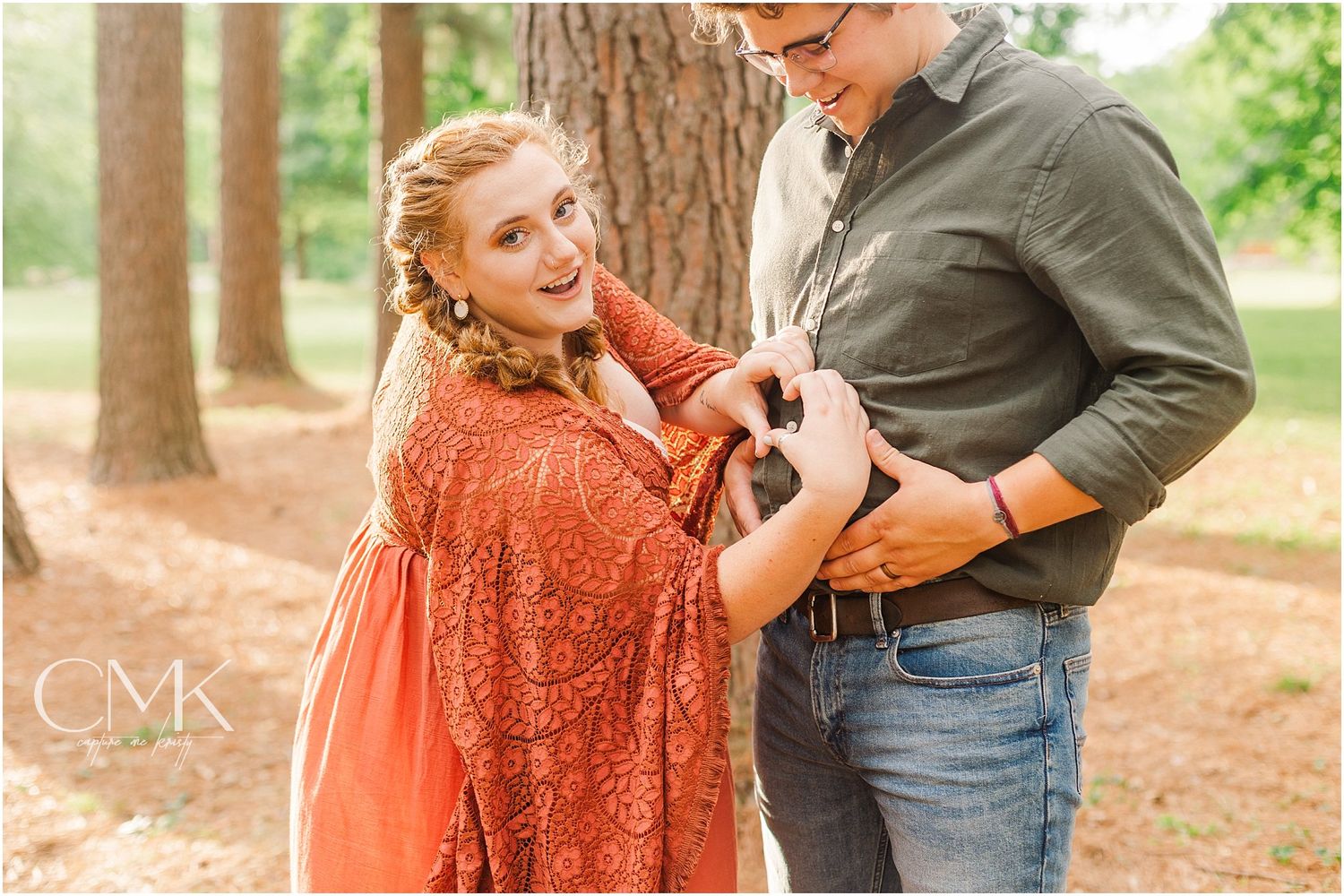 Playful maternity photo of couple interacting in a pine forest setting.