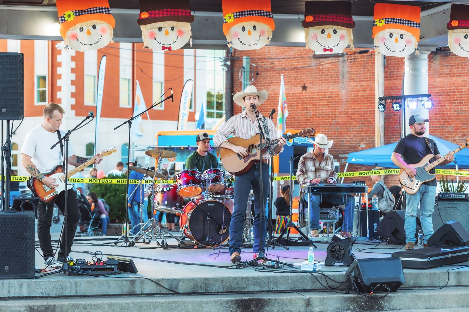 Band performing on outdoor stage with orange snowman decorations hanging above.