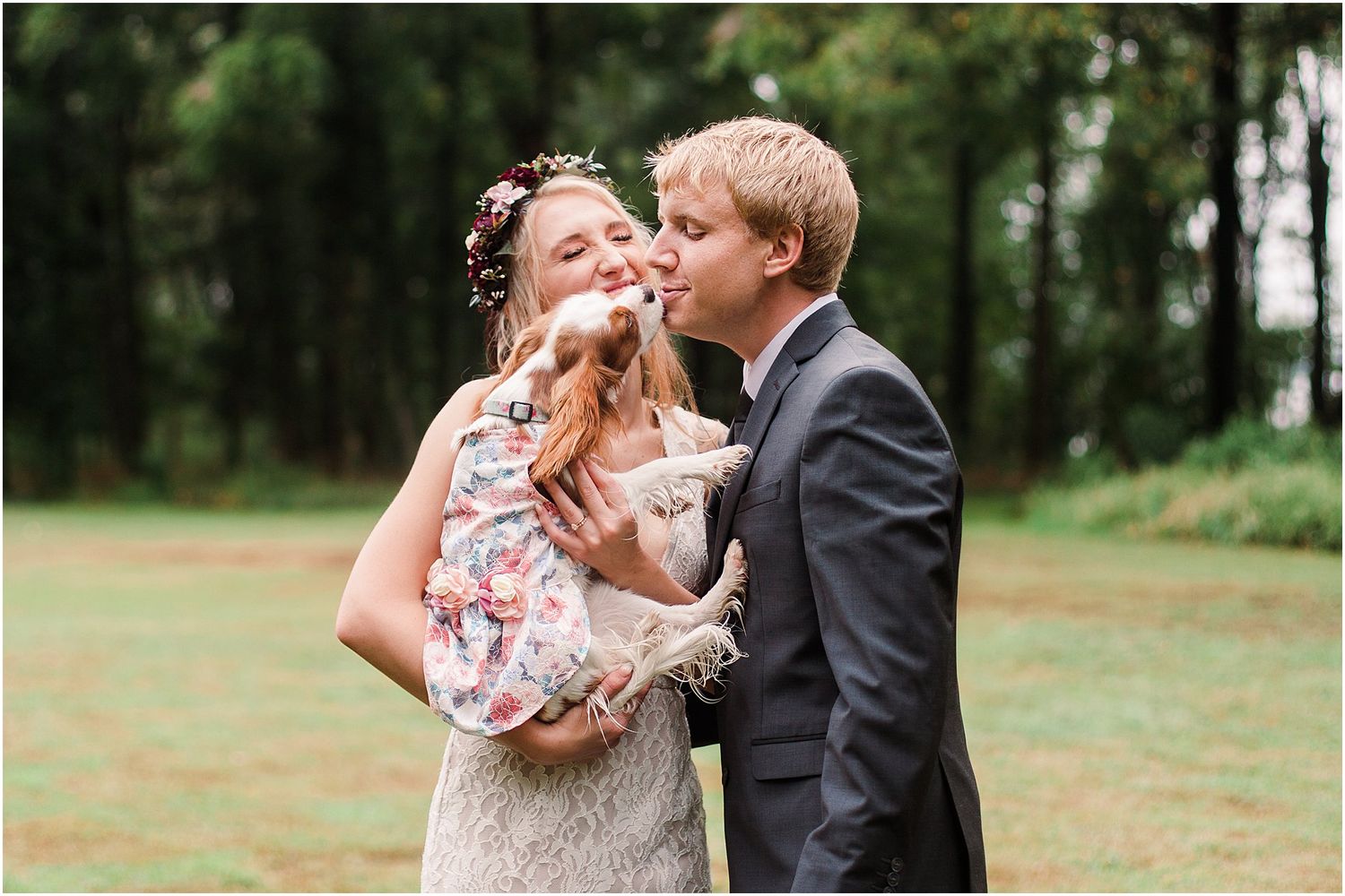 A couple shares a joyful moment with their small dog during their outdoor wedding celebration.