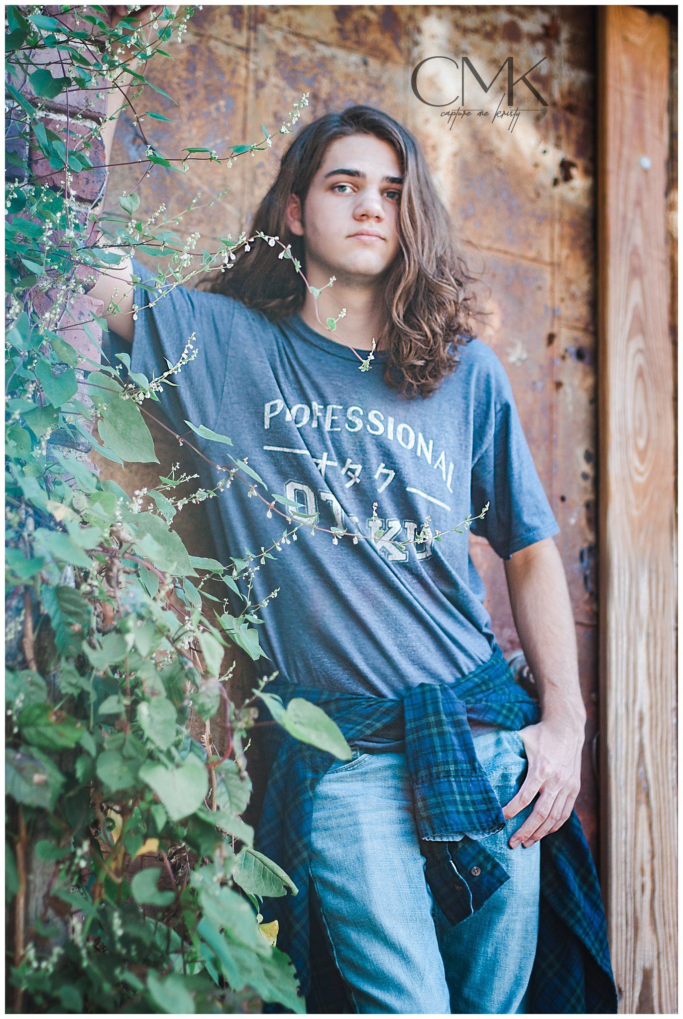 Person in navy t-shirt with text standing against rustic wall with climbing vines.