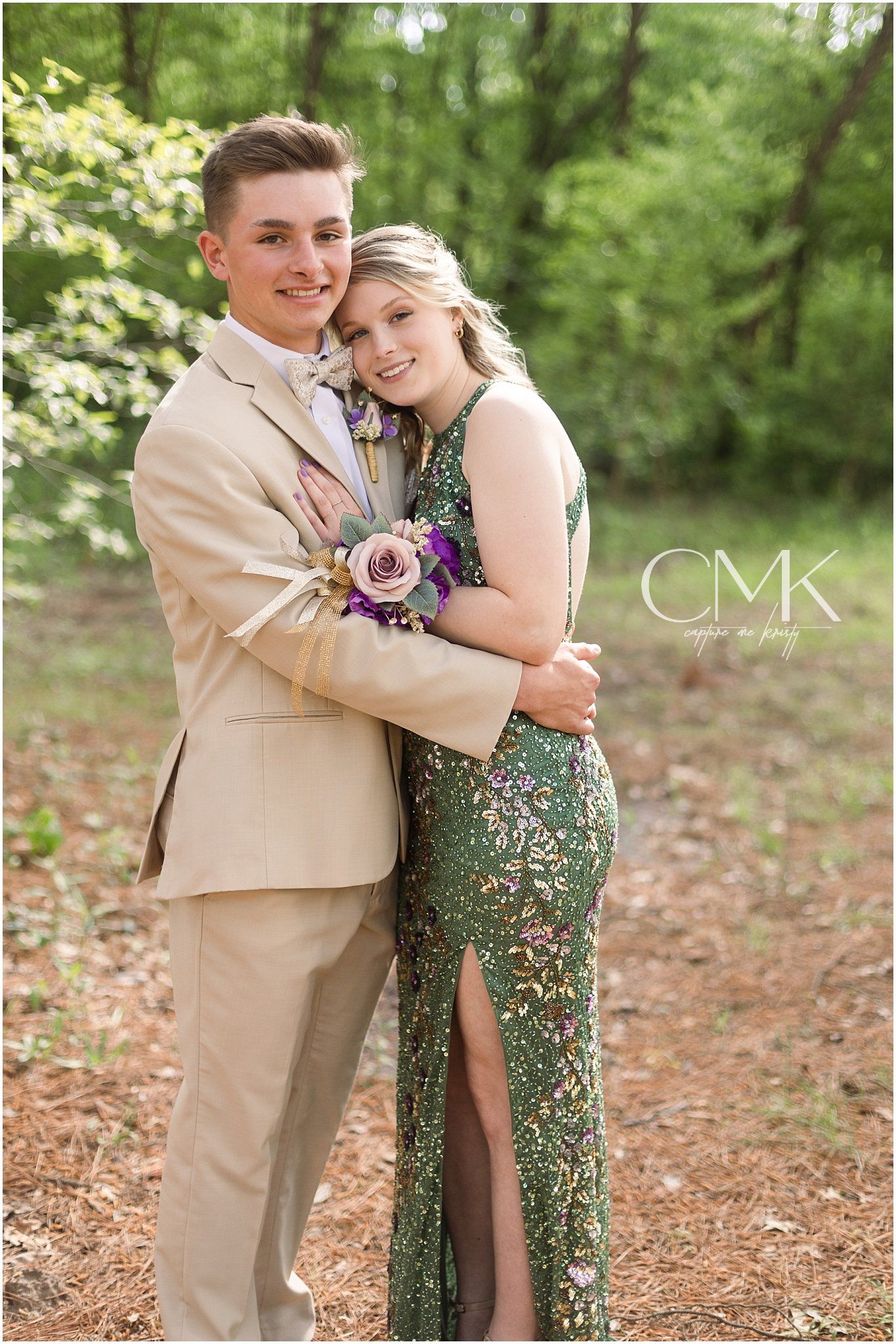 Formal couple in a forest setting with green sequined gown and tan suit sharing an embrace.