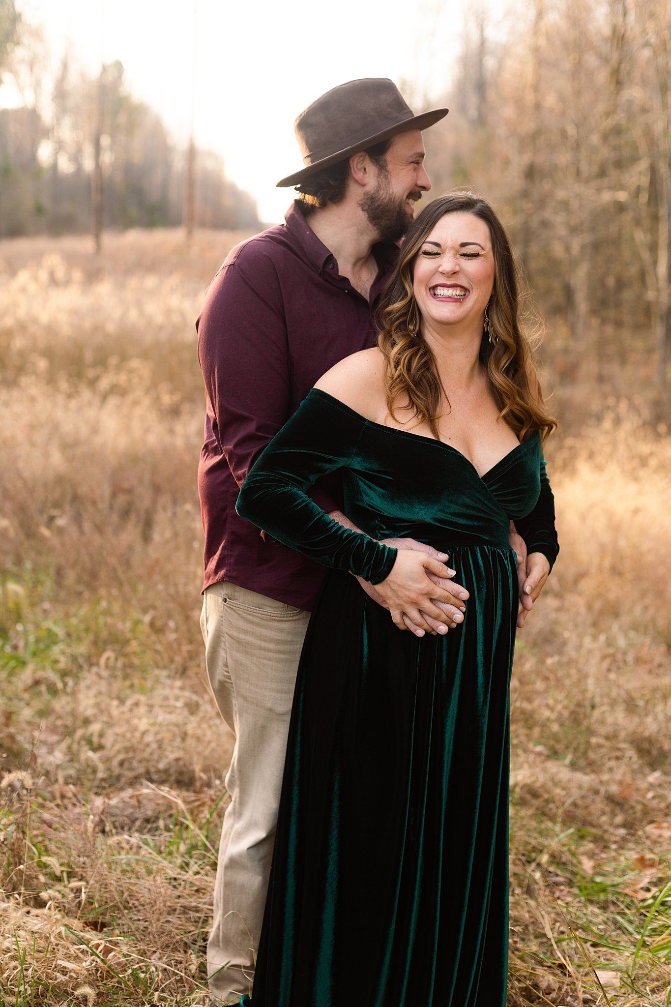 Natural maternity moment captured with couple laughing in fall field setting.