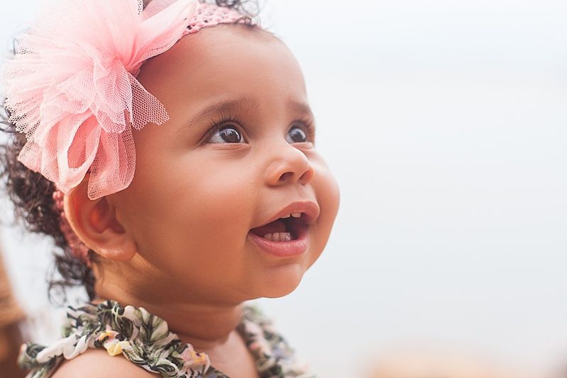 Close up portrait of joyful baby wearing pink bow headband and floral dress looking upward.